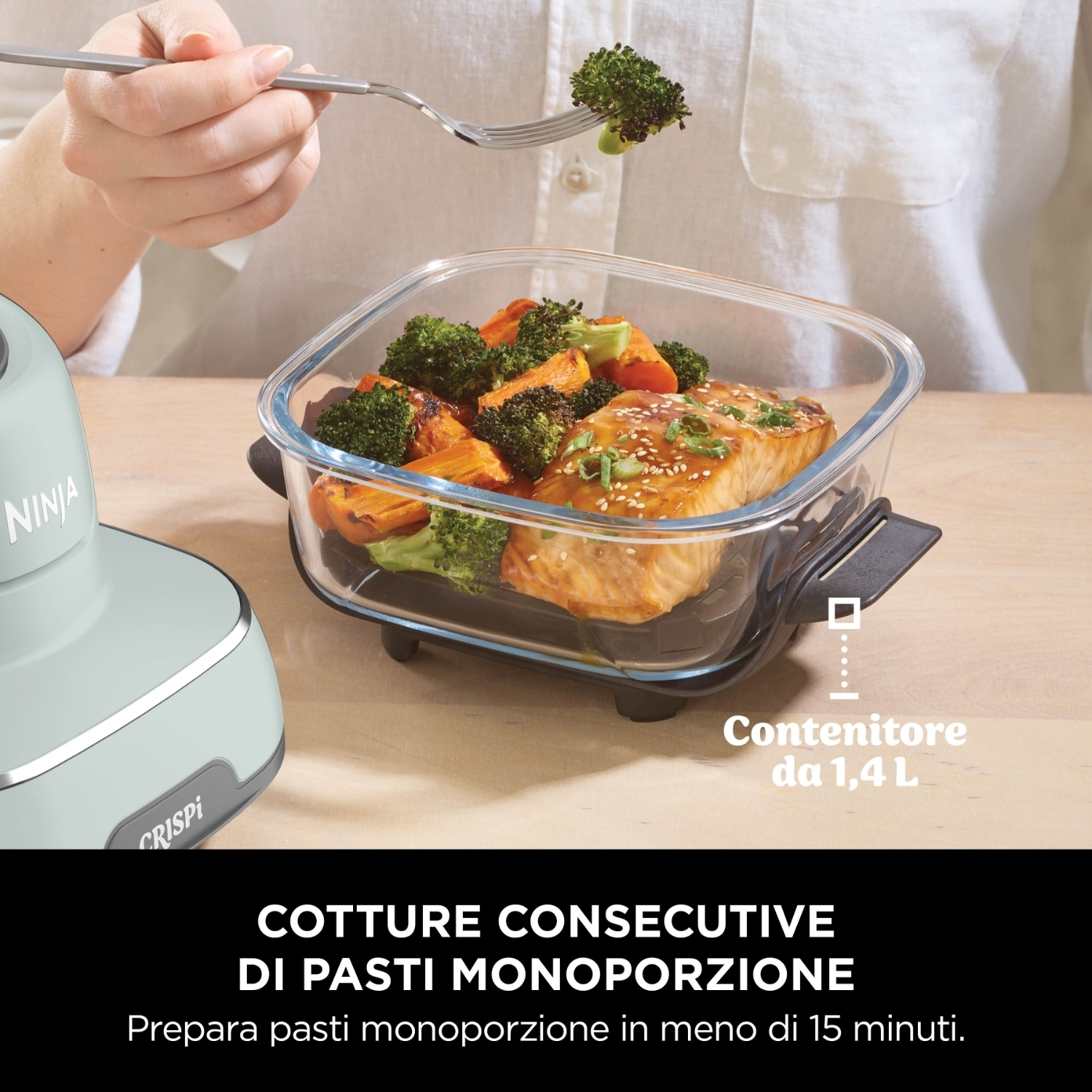 Una persona tiene broccoli con una forchetta sopra un contenitore di vetro con salmone, broccoli e patate dolci. Ninja Crispi è a sinistra.