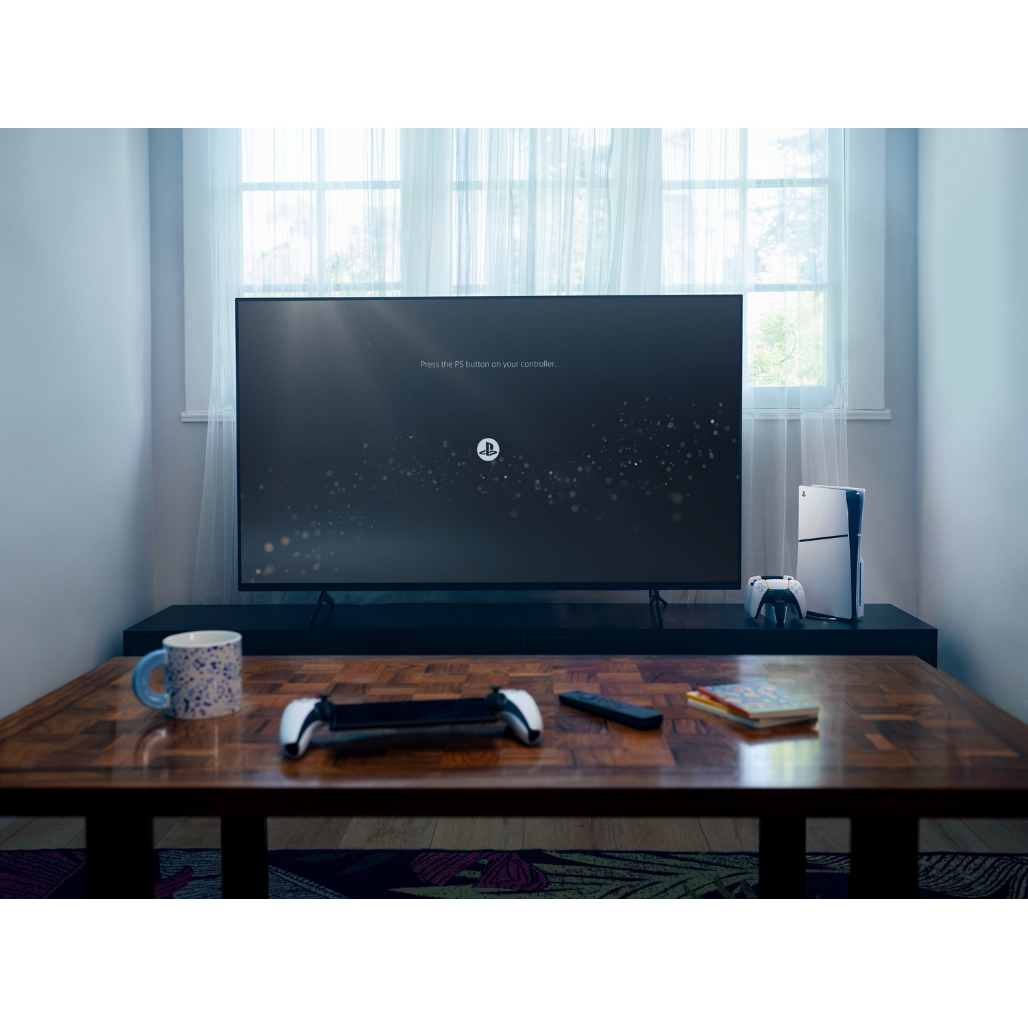 Living room with a TV, PS5, controllers, and a wooden table. The TV screen displays the PlayStation logo.