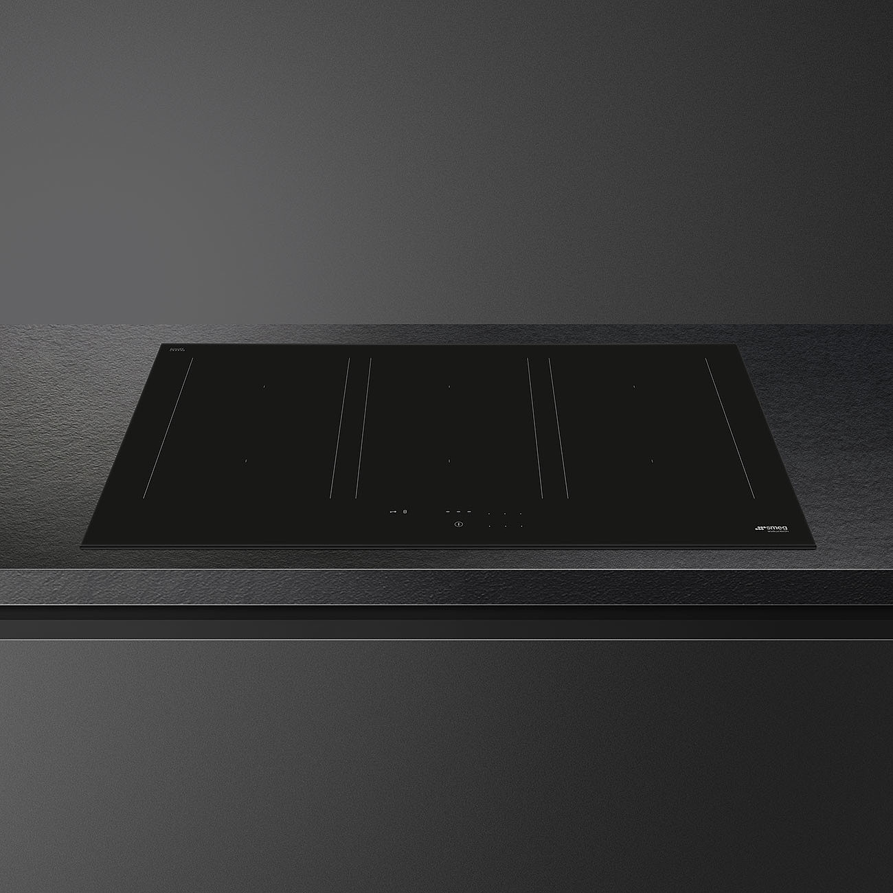 Ein schwarzes Smeg-Induktionskochfeld auf einer grauen Arbeitsplatte. Das Kochfeld hat mehrere Brenner mit Touch-Bedienelementen. Der Hintergrund ist grau.