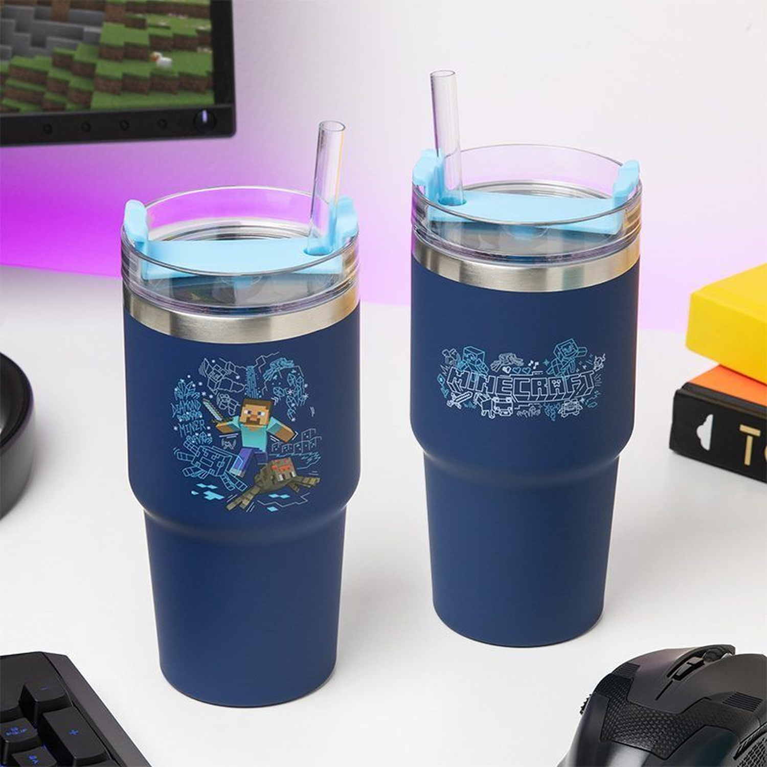 Two blue Minecraft-themed tumblers with straws on a white surface, near a keyboard, mouse, and monitor.