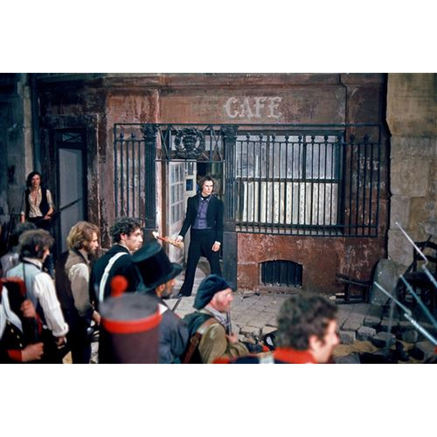 Un homme se tient devant un café avec un groupe de personnes. Panneau de café au-dessus de la porte. Gens en vêtements historiques.