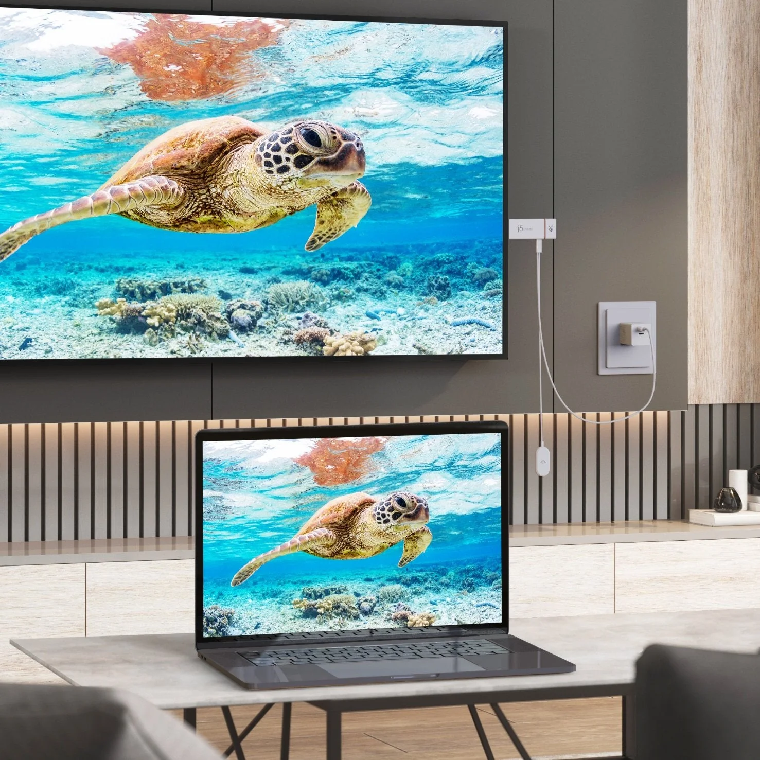Egy tengeri teknős úszik az óceánban, egy TV-n és laptopon megjelenítve. Egy fehér eszköz van a TV-hez csatlakoztatva. Modern konyhai környezet.
