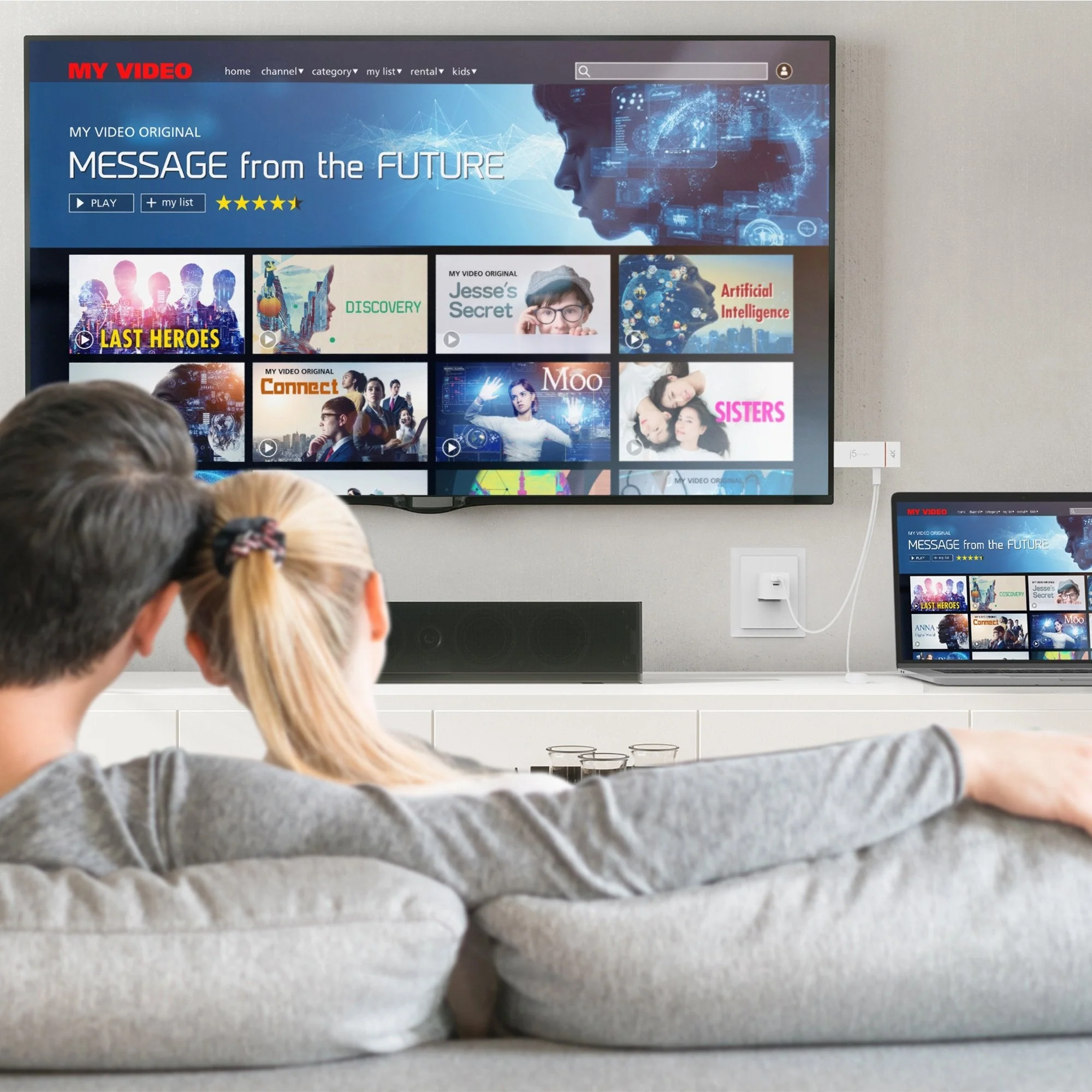 Pár tévét néz streaming szolgáltatás felülettel. Laptop ugyanazt a felületet mutatja. Hangprojektor a TV alatt.