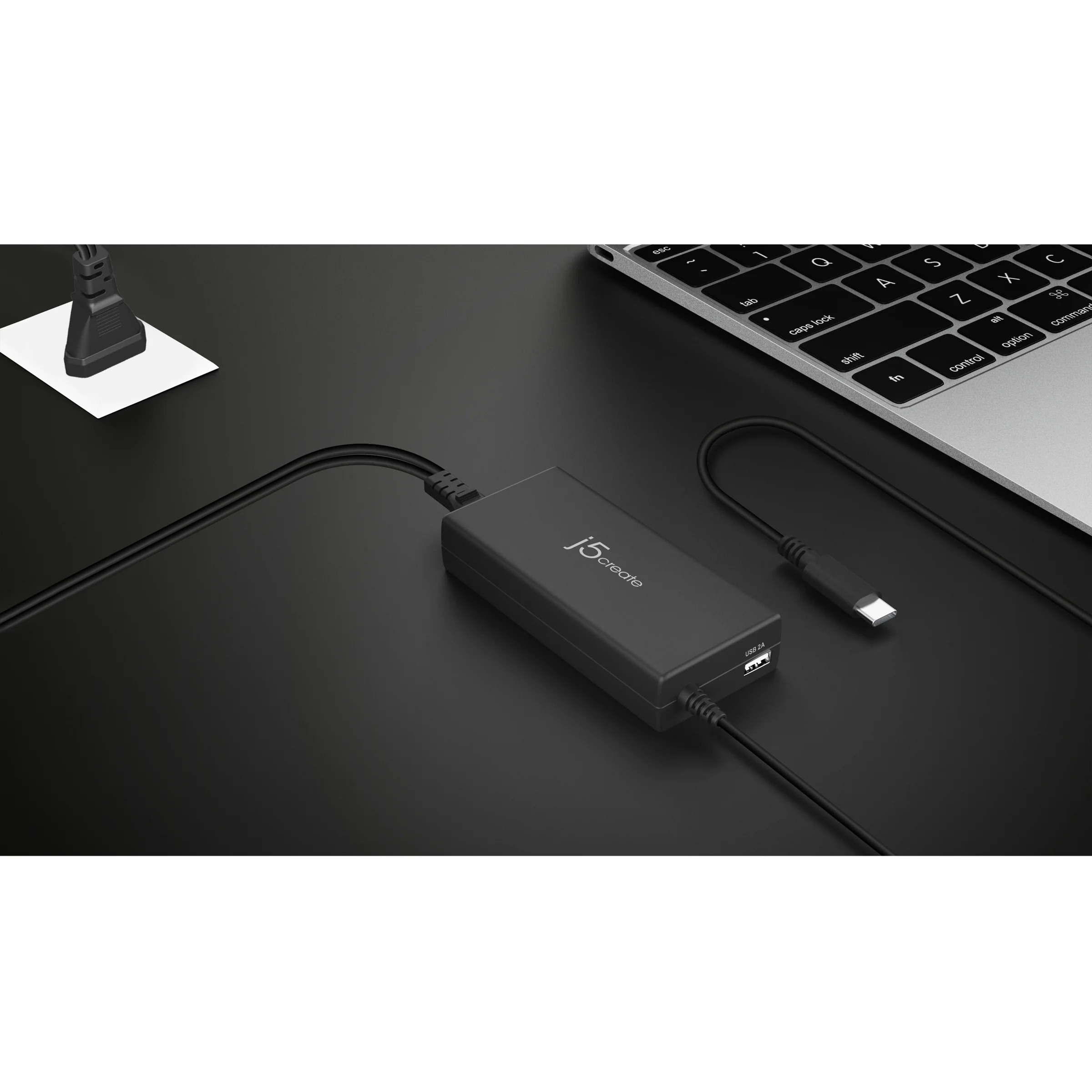 Egy fekete USB hub kábelekkel és egy USB-C kábel az asztalon, egy laptop billentyűzet mellett.