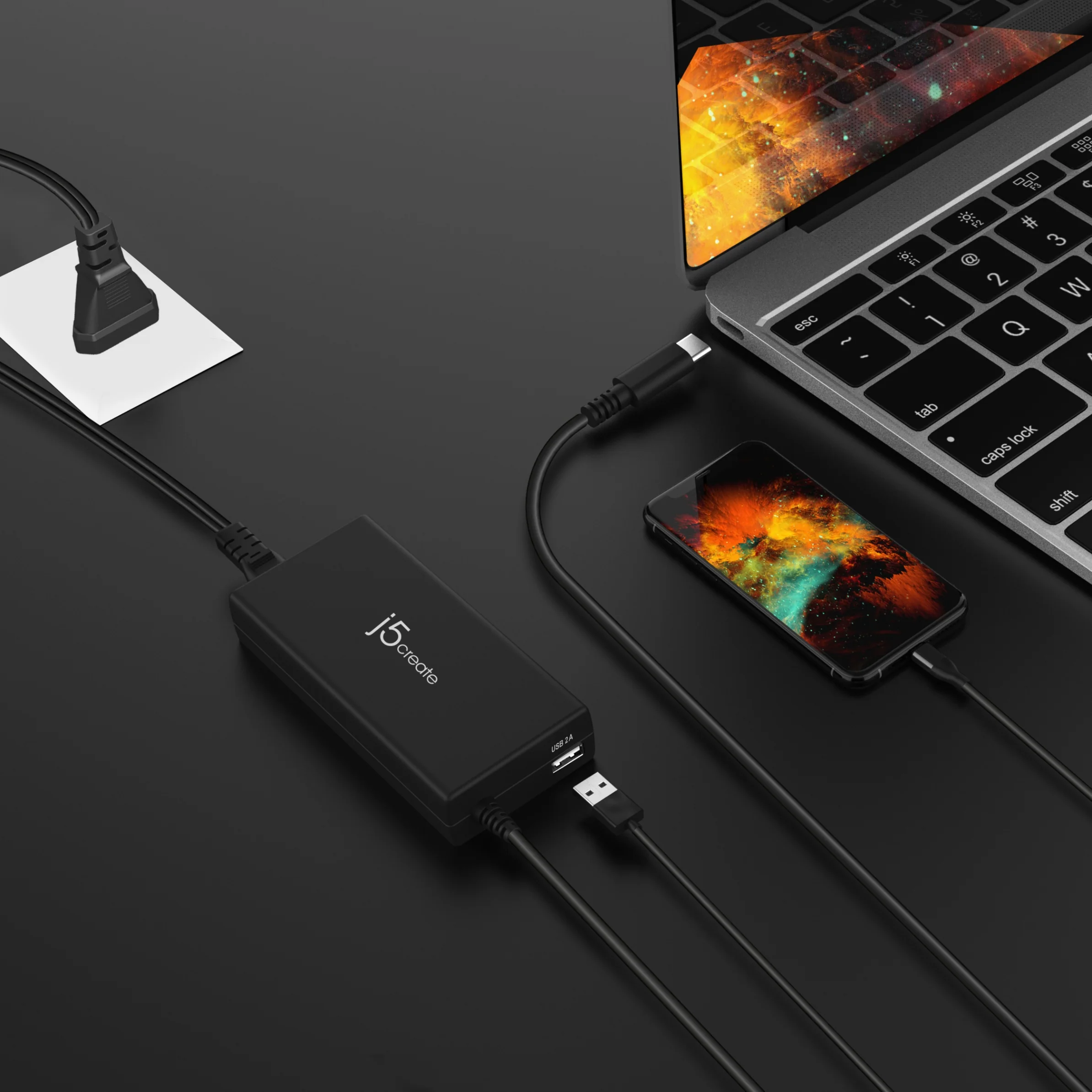 Fekete laptop, telefon és USB hub csatlakoztatva kábelekkel egy sötét felületen. A telefon színes képet mutat.