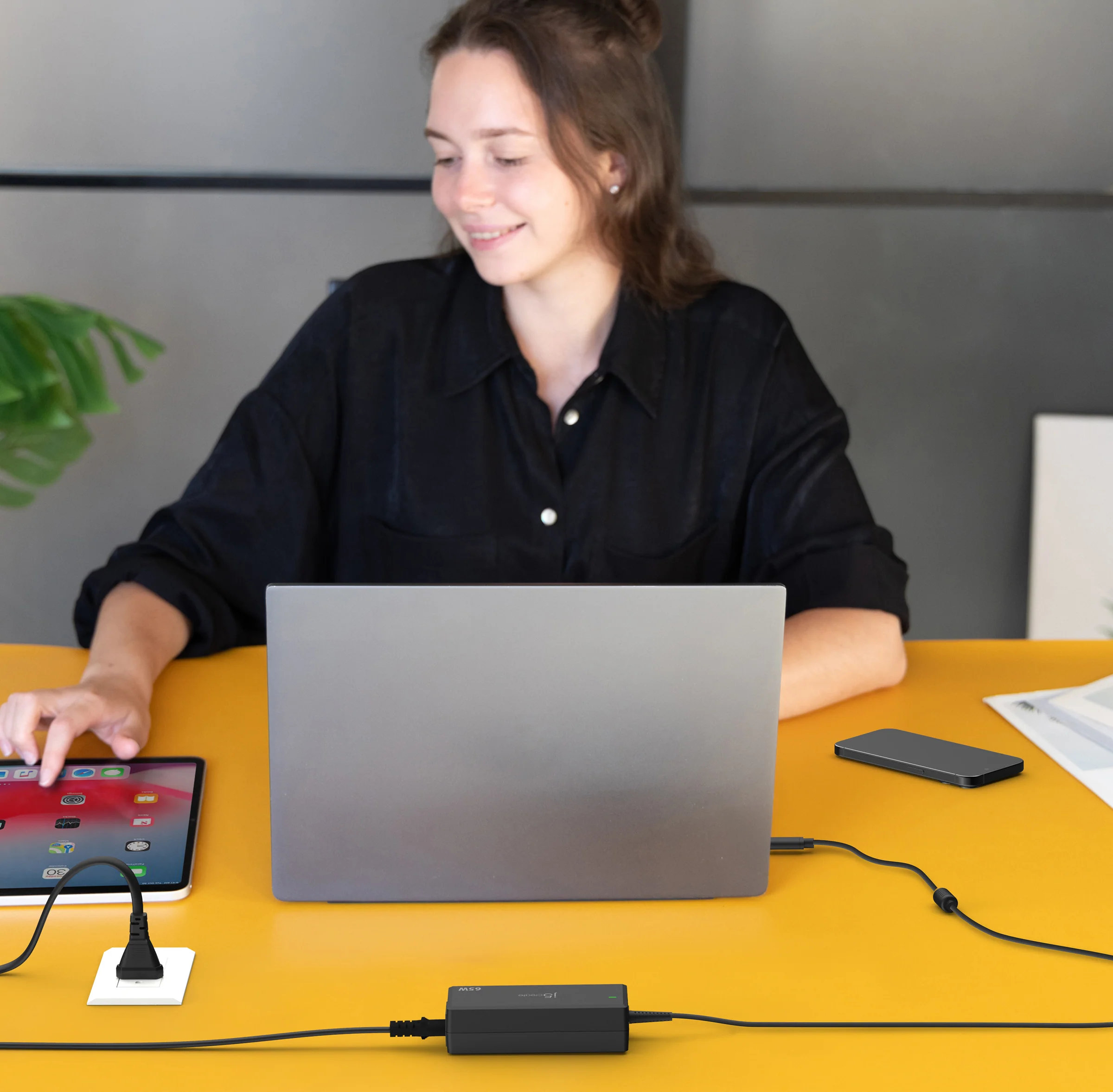 Nő laptopot és táblagépet használ. Sárga asztal, eszközökkel és adapterrel.