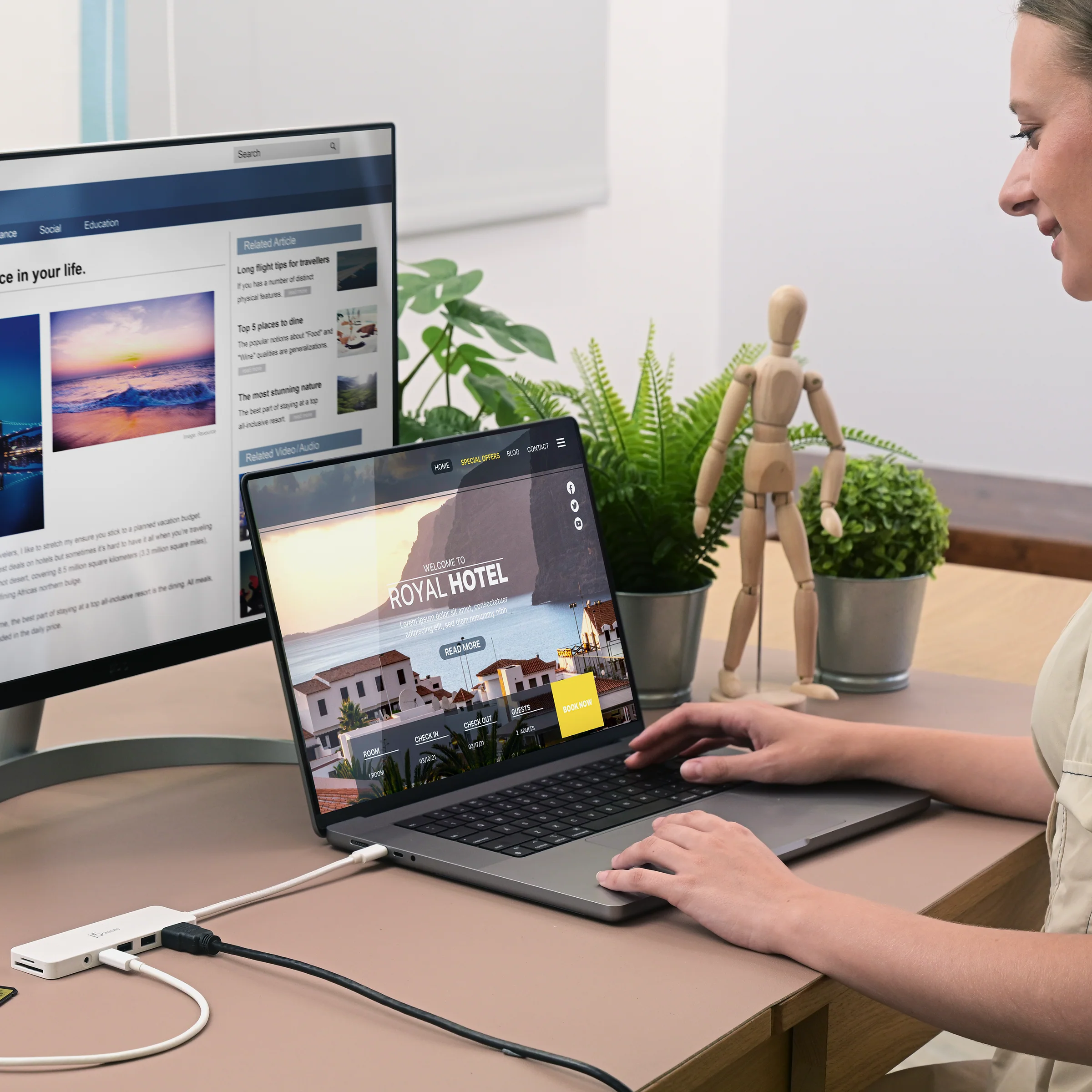 Egy nő laptopot használ. A Royal Hotel weboldala nyitva van. Egy monitor és növények láthatók.