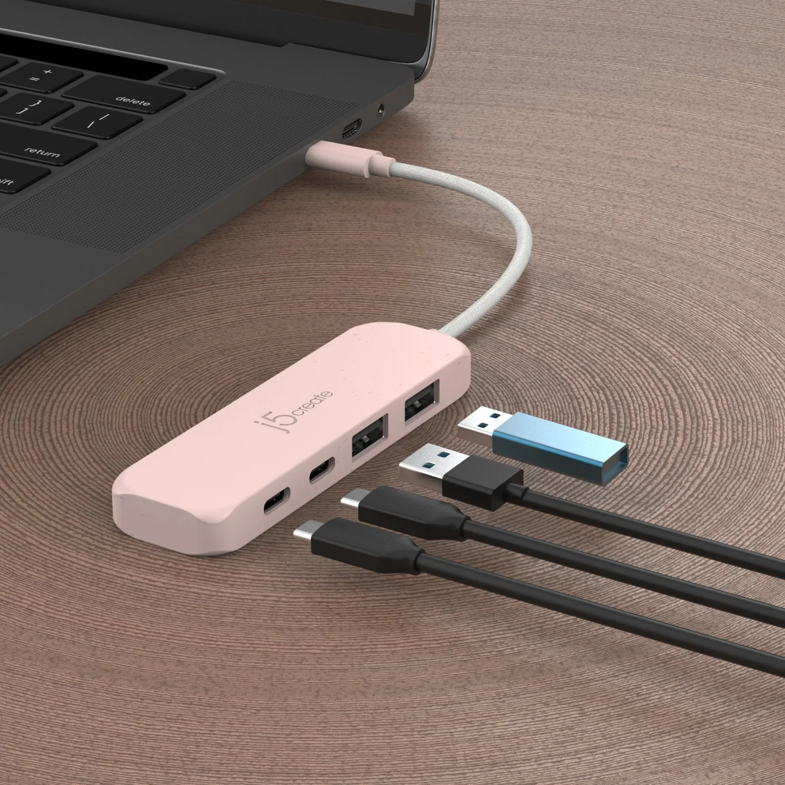 Egy rózsaszín USB-elosztó csatlakoztatva egy laptophoz. Több fekete USB-kábel és egy kék pendrive fa felületen.