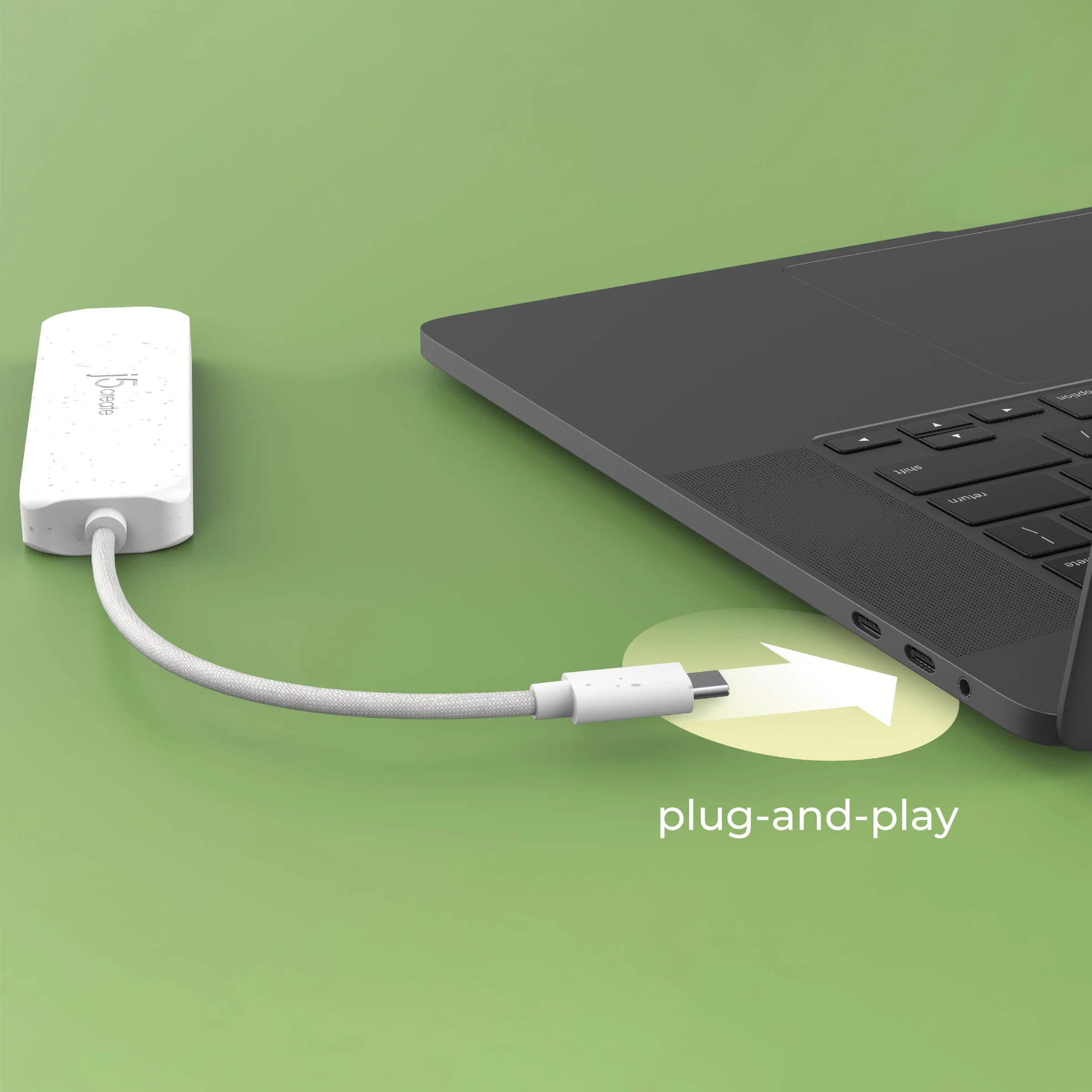 Egy fehér J5create adapter egy fehér kábellel egy MacBookhoz van csatlakoztatva, zöld háttérrel és a plug-and-play szavakkal.