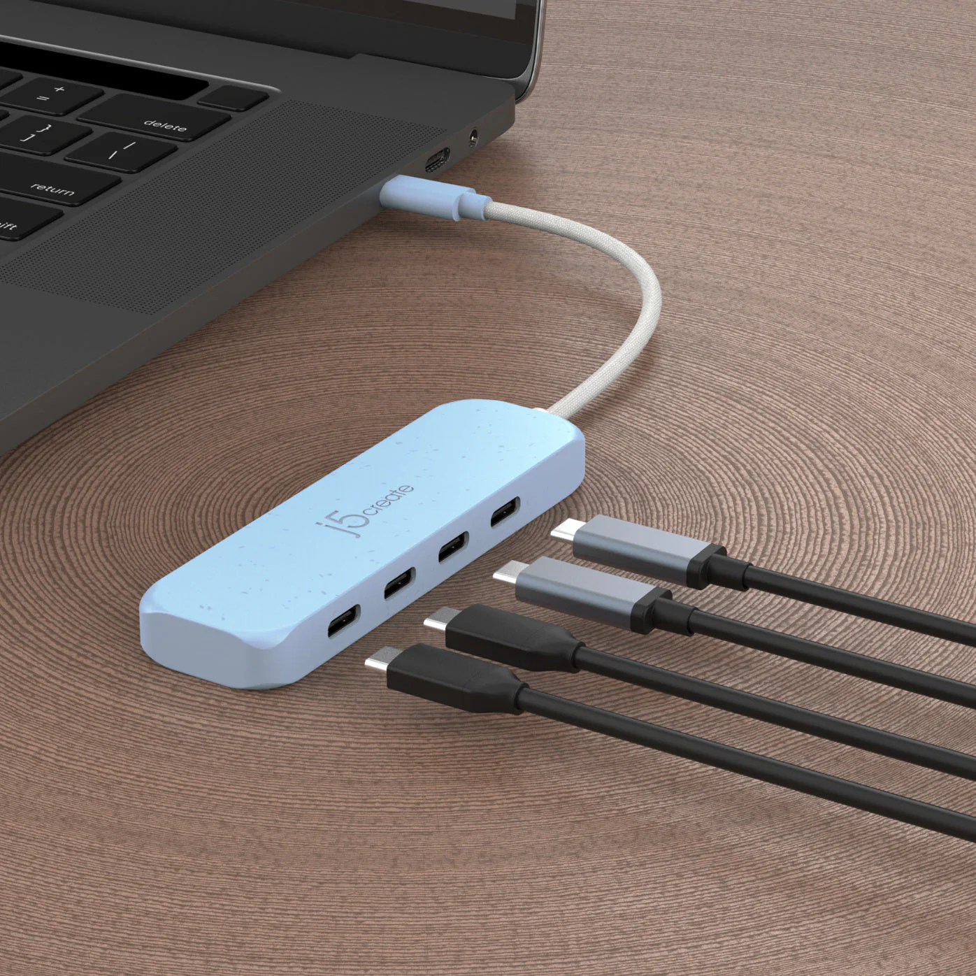 Egy kék USB-elosztó egy laptophoz csatlakoztatva. Több USB-C kábel csatlakozik az elosztóhoz, fa felületre helyezve.