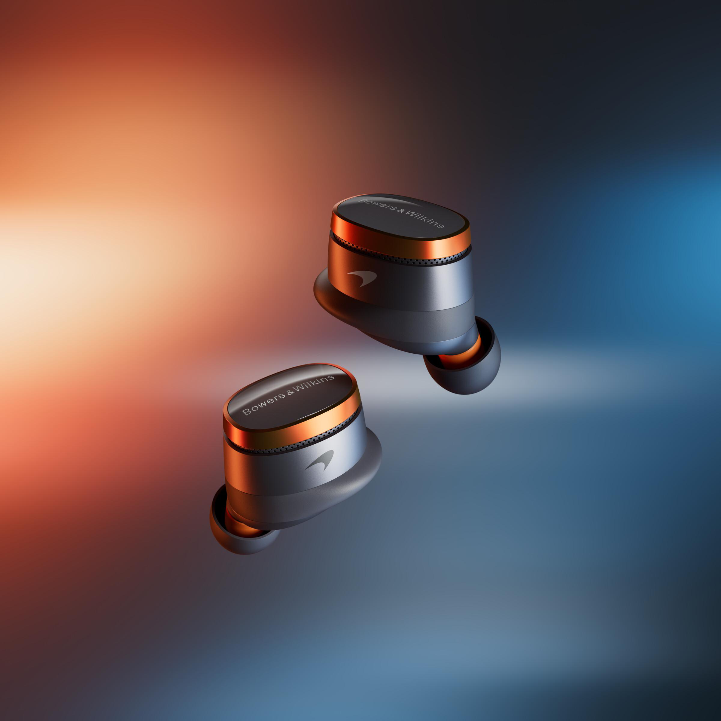Zwei Bowers & Wilkins-Ohrhörer, silber und kupferfarben, auf einem roten bis blauen Farbverlauf. McLaren-Logo sichtbar.