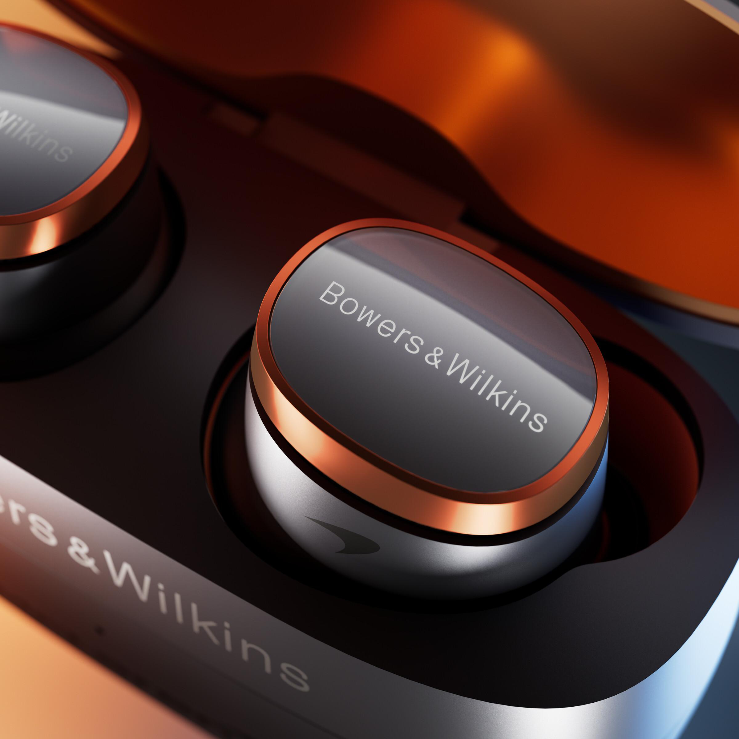 Nahaufnahme von Bowers & Wilkins-Ohrhörern. Das Gehäuse ist geöffnet und zeigt die Ohrhörer. Grau, Kupfer und Schwarz.