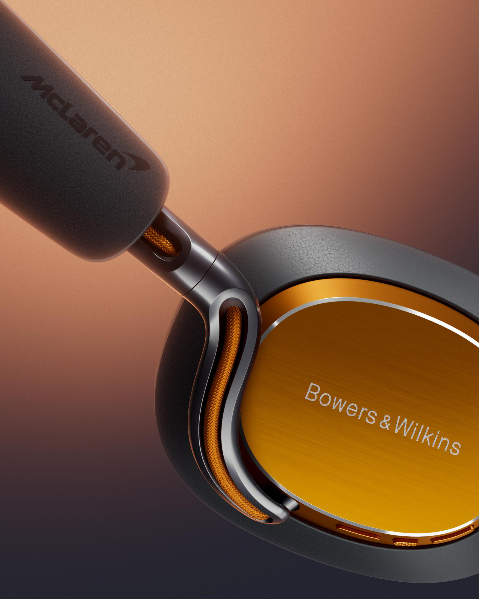 Nahaufnahme von McLaren Bowers & Wilkins Kopfhörern. Schwarze Ohrmuscheln mit orangefarbenen Akzenten und einem goldenen Panel.