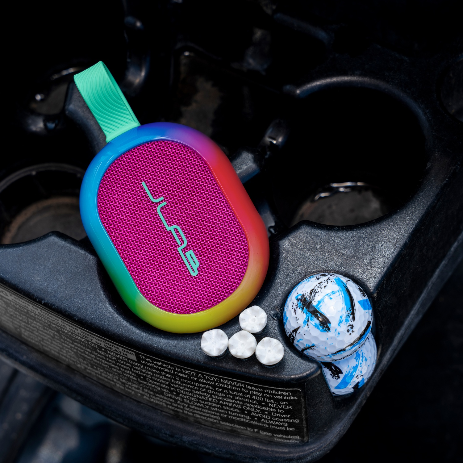 Un haut-parleur coloré, des balles de golf et des menthes reposent dans le porte-gobelet d'une voiture. Une sangle verte est attachée au haut-parleur.