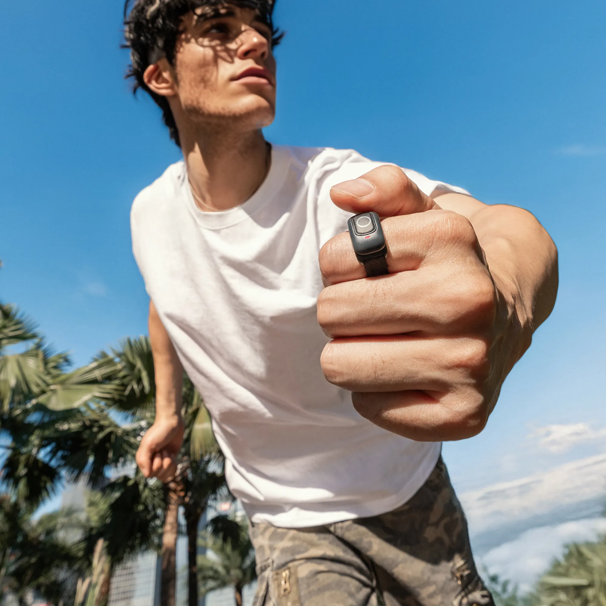 Ein Mann hält eine Hand mit einem Ring hoch. Palmen und blauer Himmel sind im Hintergrund.