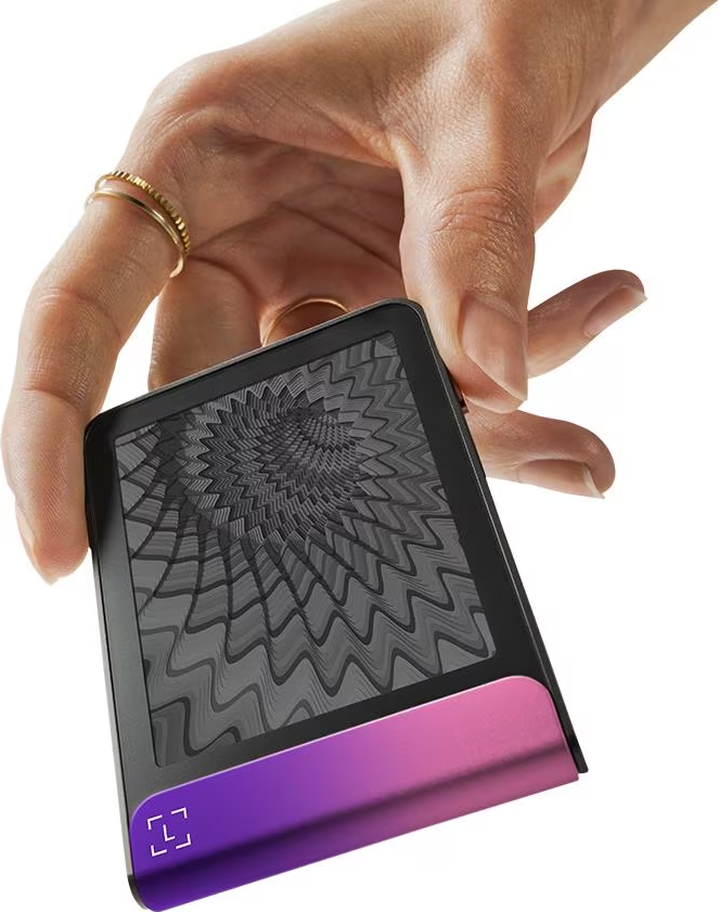 Una mano che tiene un dispositivo nero con un gradiente rosa-viola sul fondo. Lo schermo mostra un motivo grigio a spirale. Due anelli alle dita.