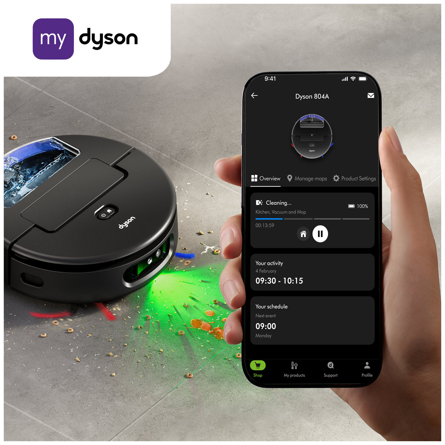 Een Dyson robotstofzuiger staat op een grijze vloer. De telefoon toont de instellingen. De telefoon wordt vastgehouden.