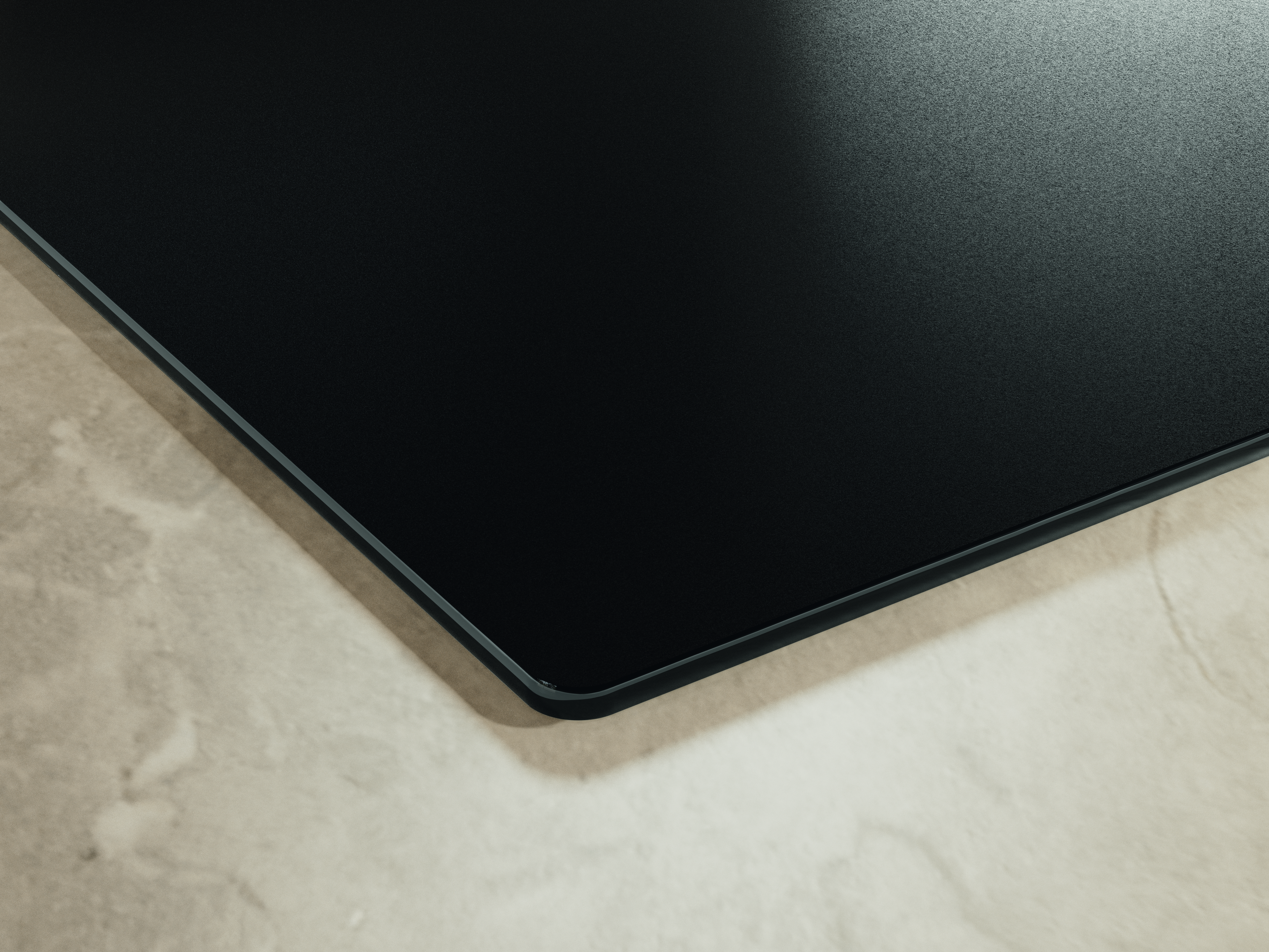 Zbliżenie czarnej, teksturowanej powierzchni z zaokrąglonym rogiem, umieszczone na beżowej, marmuropodobnej powierzchni.