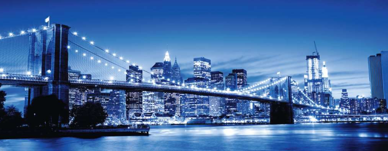 Brooklyn Bridge bei Nacht, Lichter spiegeln sich im Wasser. Skyline im Hintergrund mit beleuchteten Gebäuden.