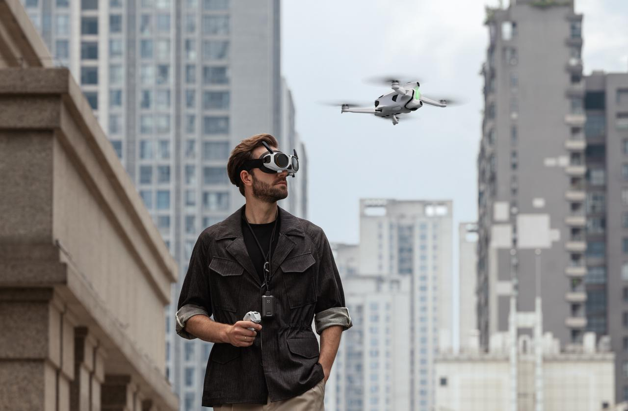 Gözlük takan bir adam şehirde bir dronu kullanıyor. Arka planda binalar var ve dron uçuşta.