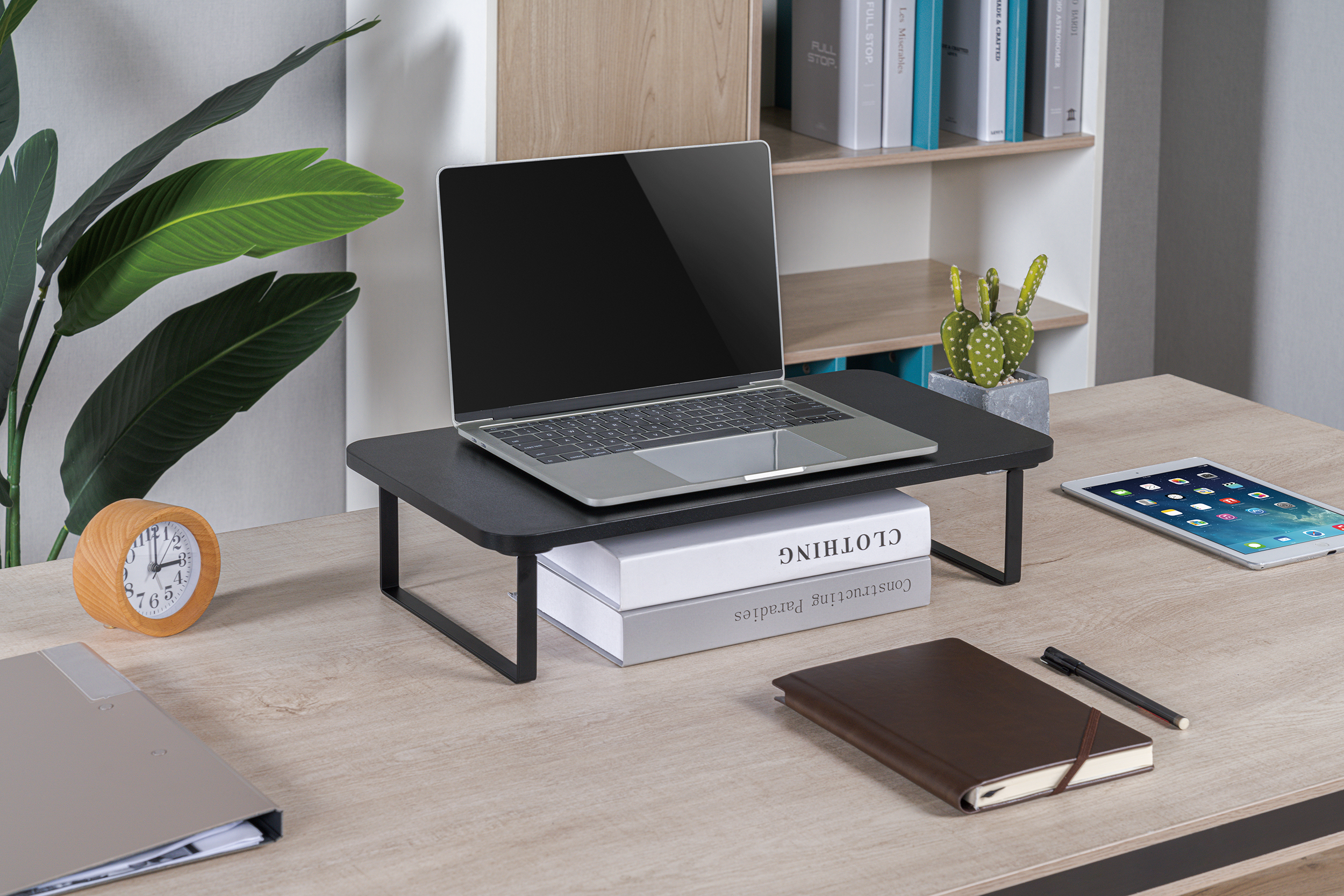 Egy asztal laptop-pal, könyvekkel, órával és iPaddel. Egy növény a háttérben.