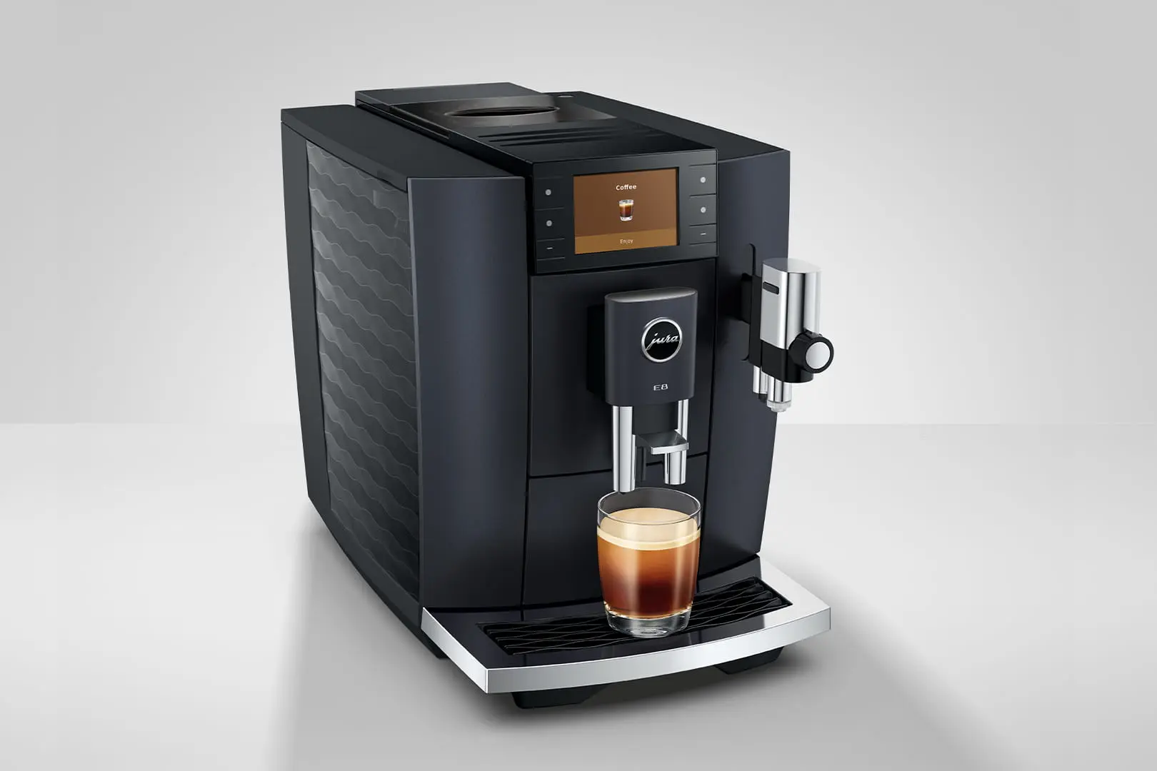 Macchina da caffè Jura nera con tazza di caffè sullo schermo, un bicchiere di caffè sotto l'erogatore.