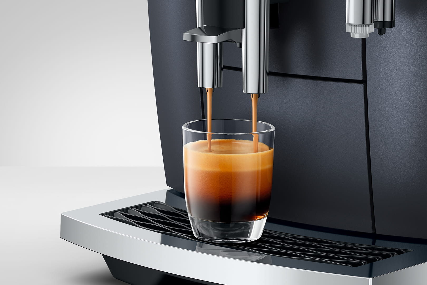 Macchina per espresso che eroga caffè in un bicchiere. La macchina è nera e argento, il caffè ha la crema.