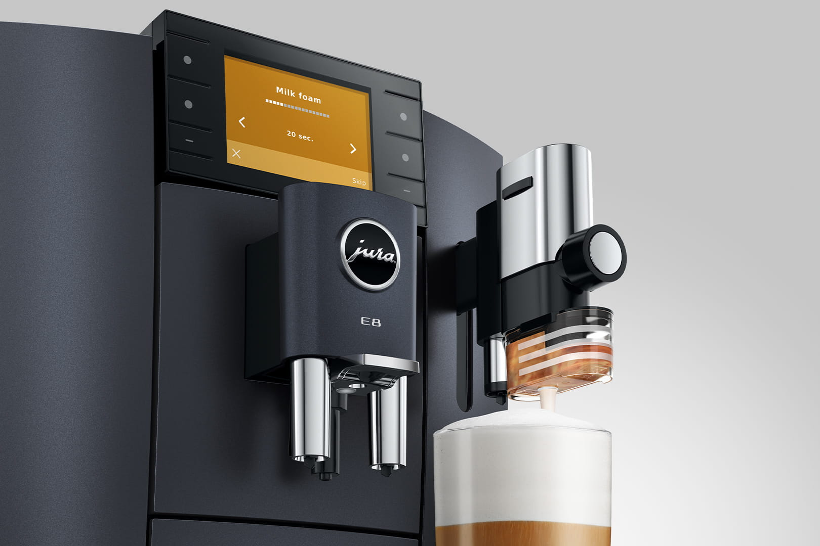 Una macchina da caffè Jura E8 nera. Si sta facendo schiuma di latte. Un bicchiere di caffè con schiuma di latte è davanti.