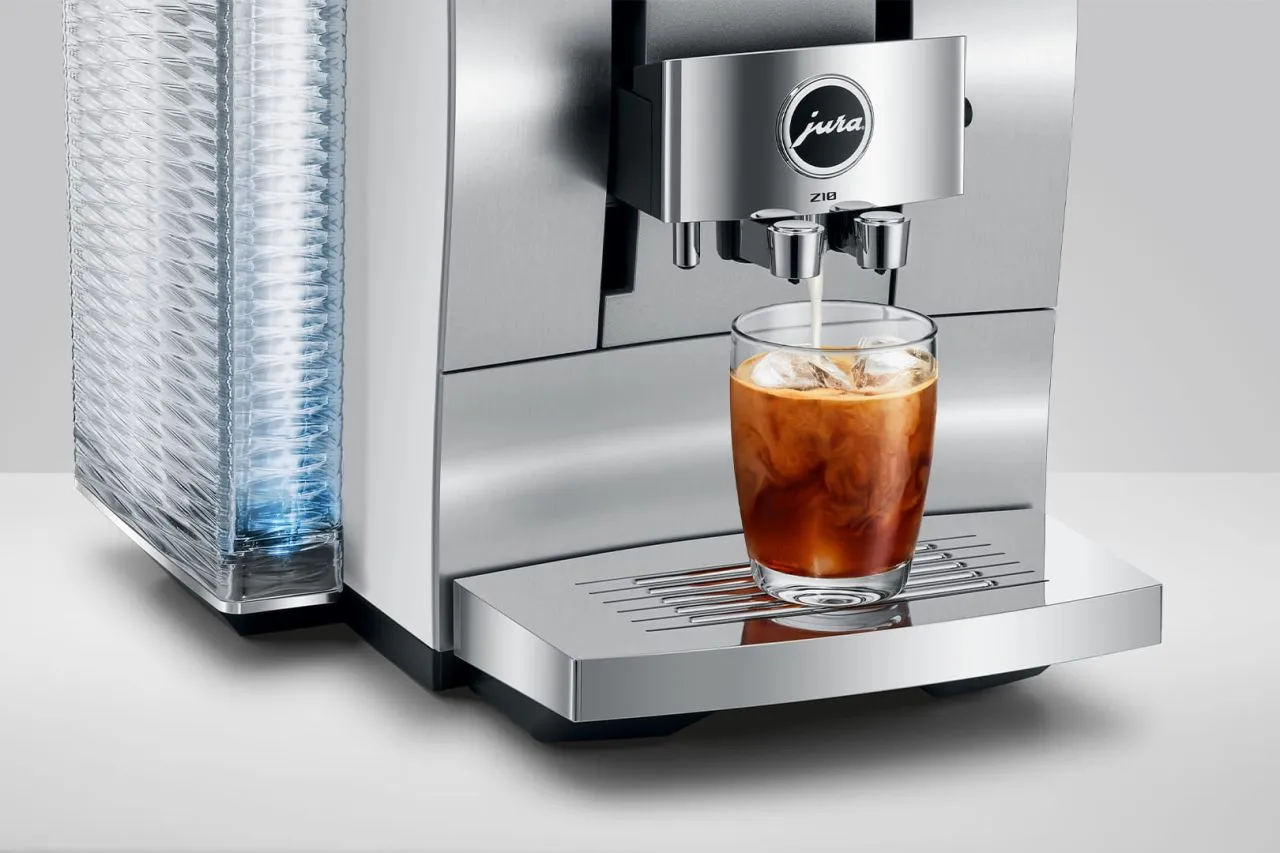 Una macchina da caffè versa latte in un bicchiere con cubetti di ghiaccio. Una pila di tazze a sinistra.