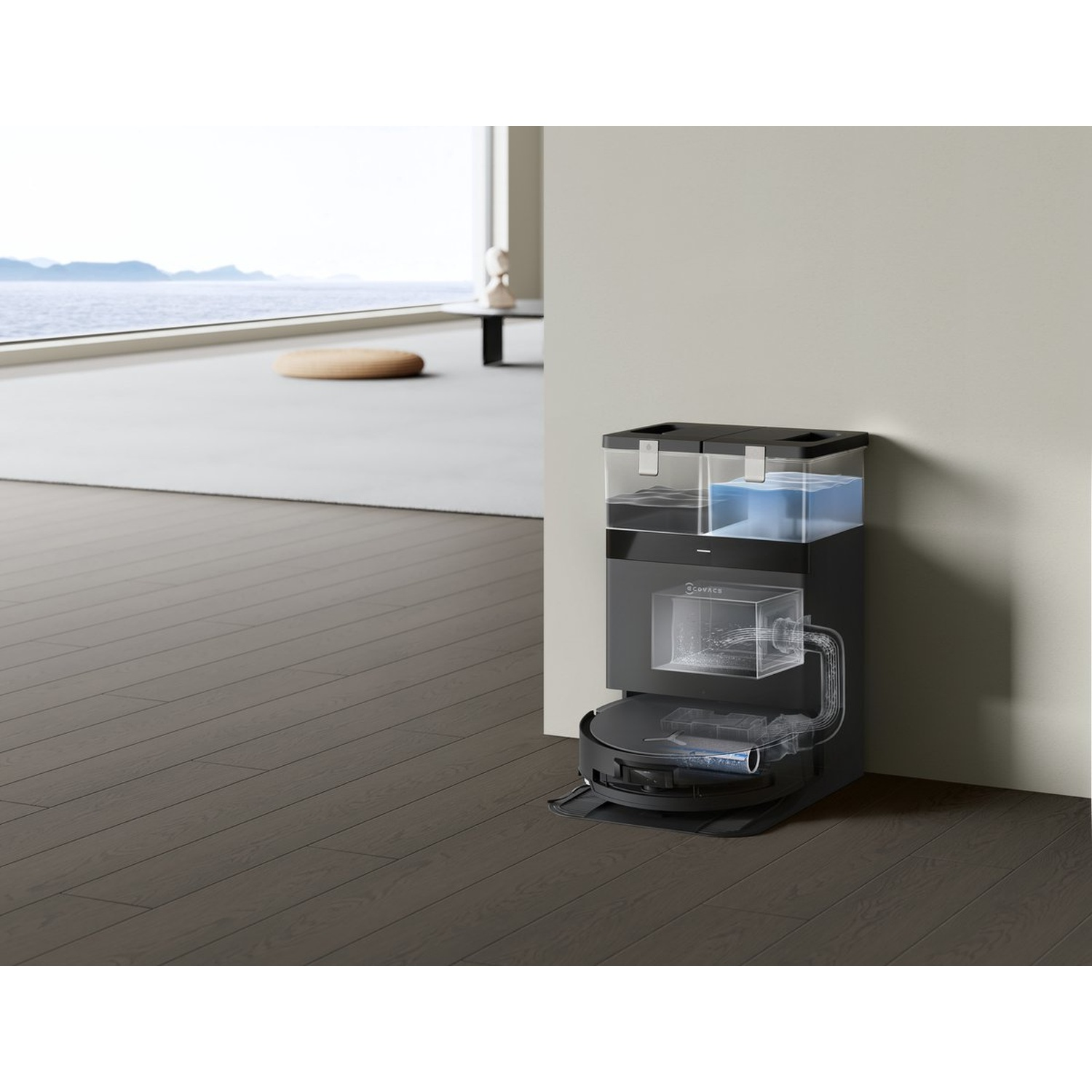 Un robot aspirateur noir et une station d'accueil se trouvent dans une pièce moderne. La station a des réservoirs d'eau. Une fenêtre donne sur une vue sur la mer.