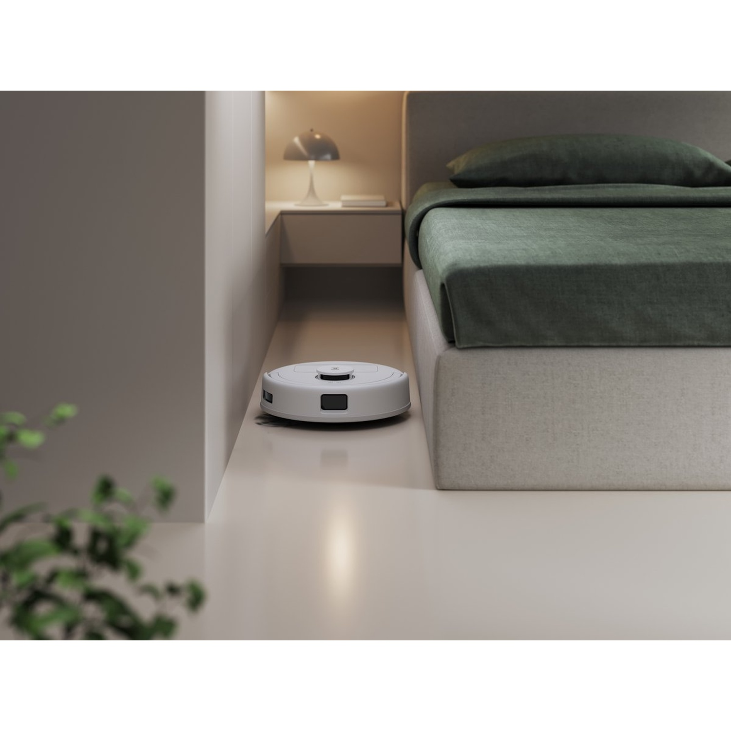 Un aspirateur robot blanc nettoie le sol à côté d'un lit avec des draps verts. Une table de chevet et une lampe sont en arrière-plan.