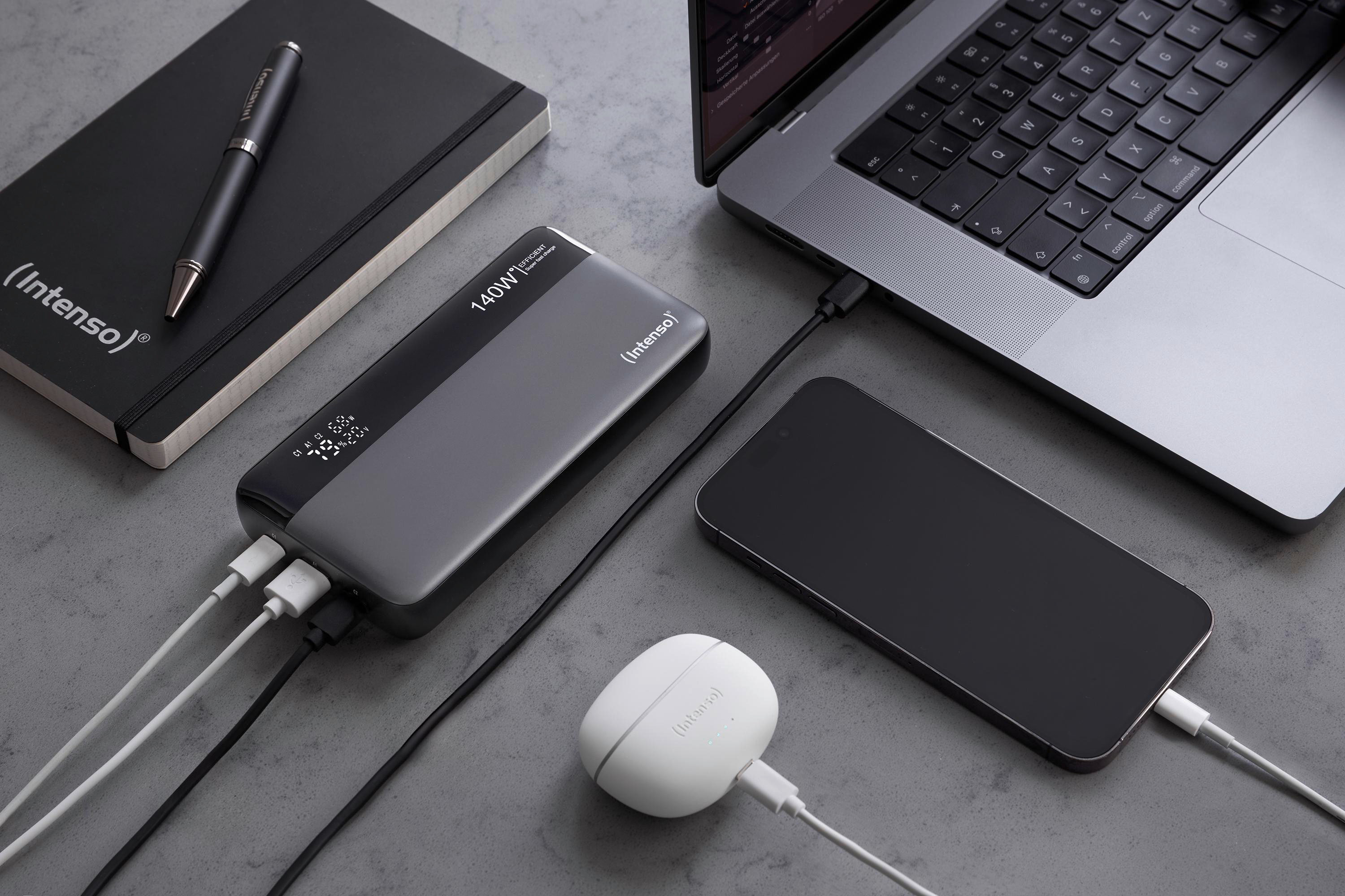 Laptop, Telefon, Powerbank, Stift und Ohrhörer auf grauem Untergrund. Alle werden geladen.