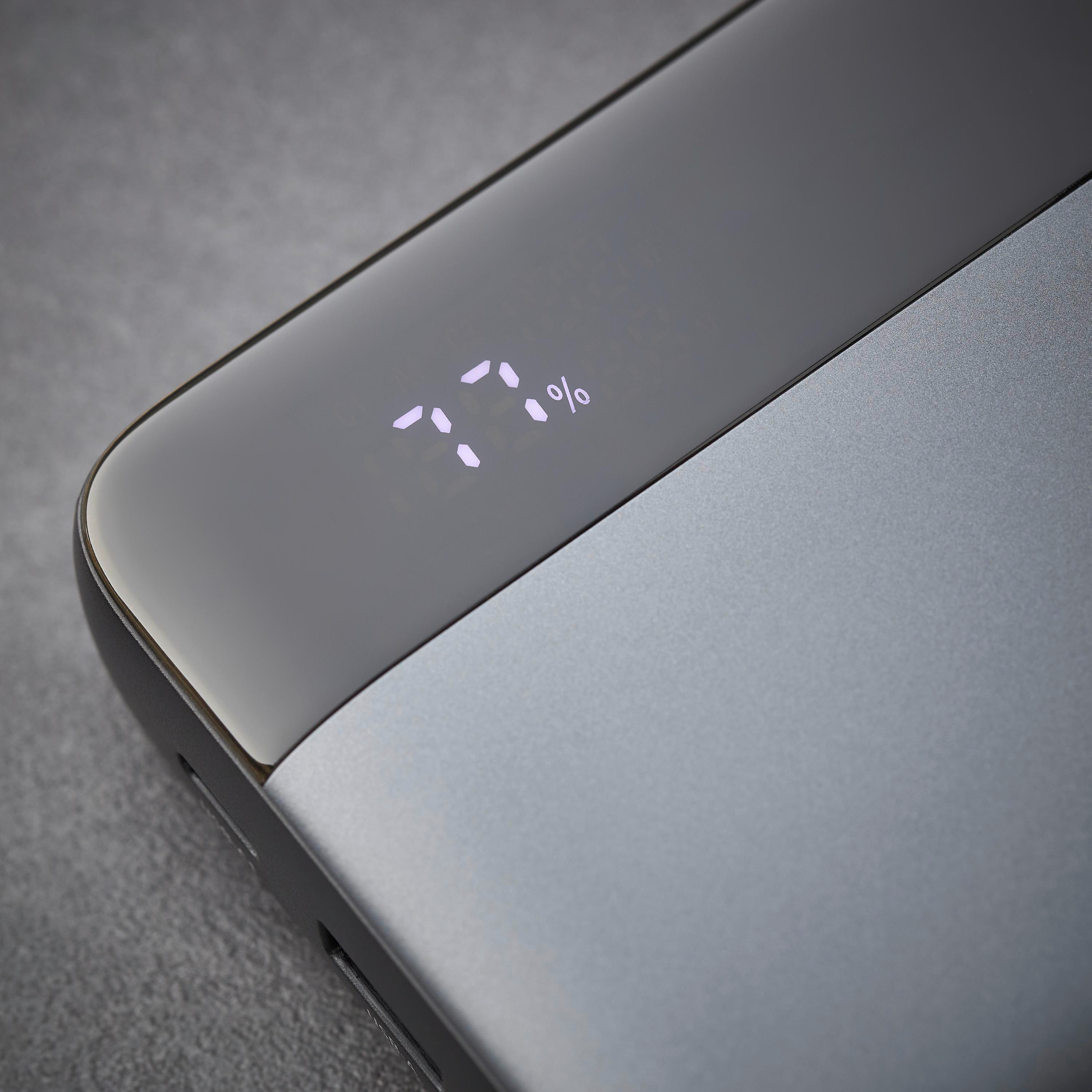 Nahaufnahme einer Powerbank mit 77 % Akku. Das Gerät ist grau mit glänzend schwarzer Oberseite. Der Hintergrund ist grau.