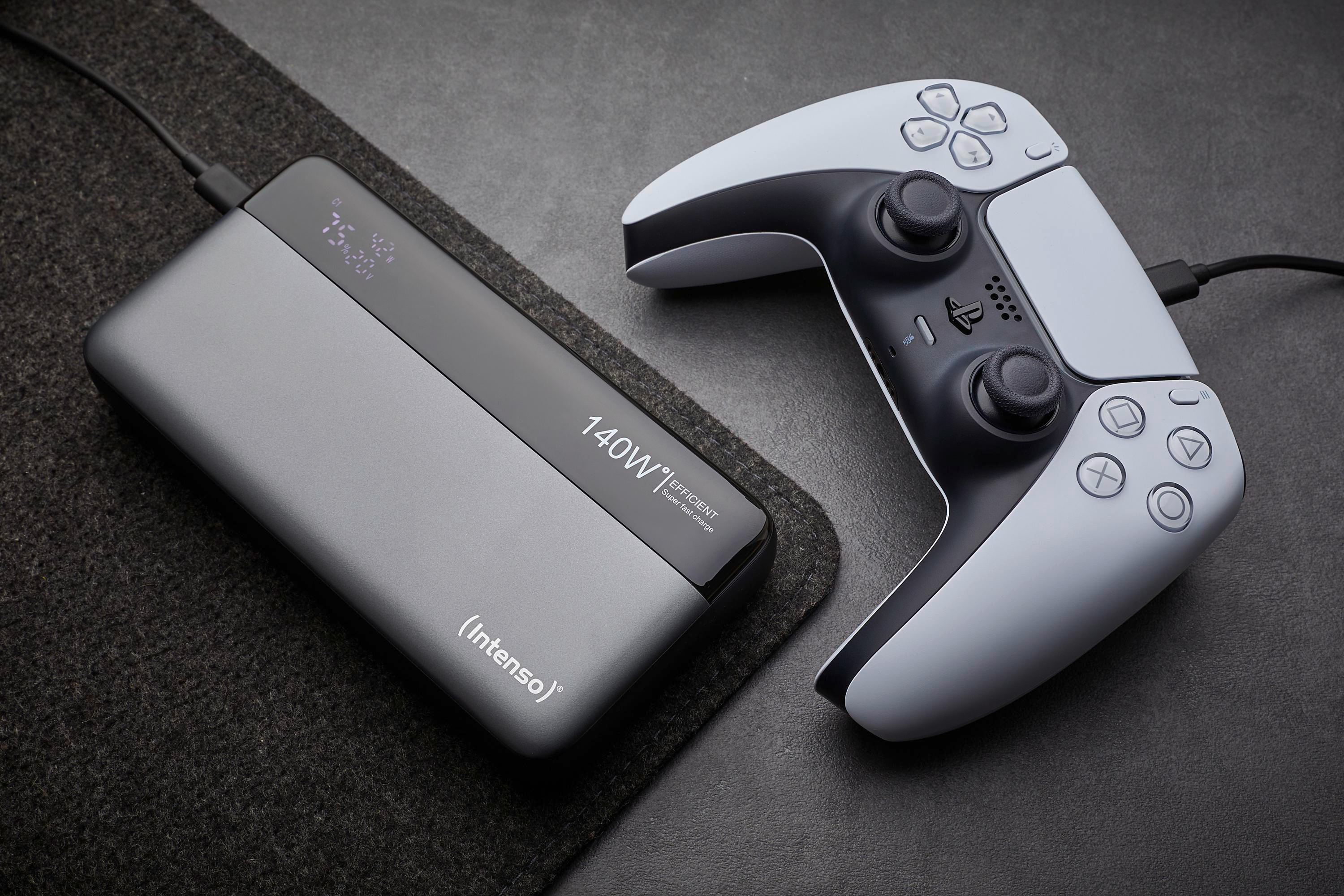 Eine graue Powerbank und ein weiß-schwarzer Game-Controller liegen auf einer dunklen Oberfläche. Die Powerbank lädt den Controller.