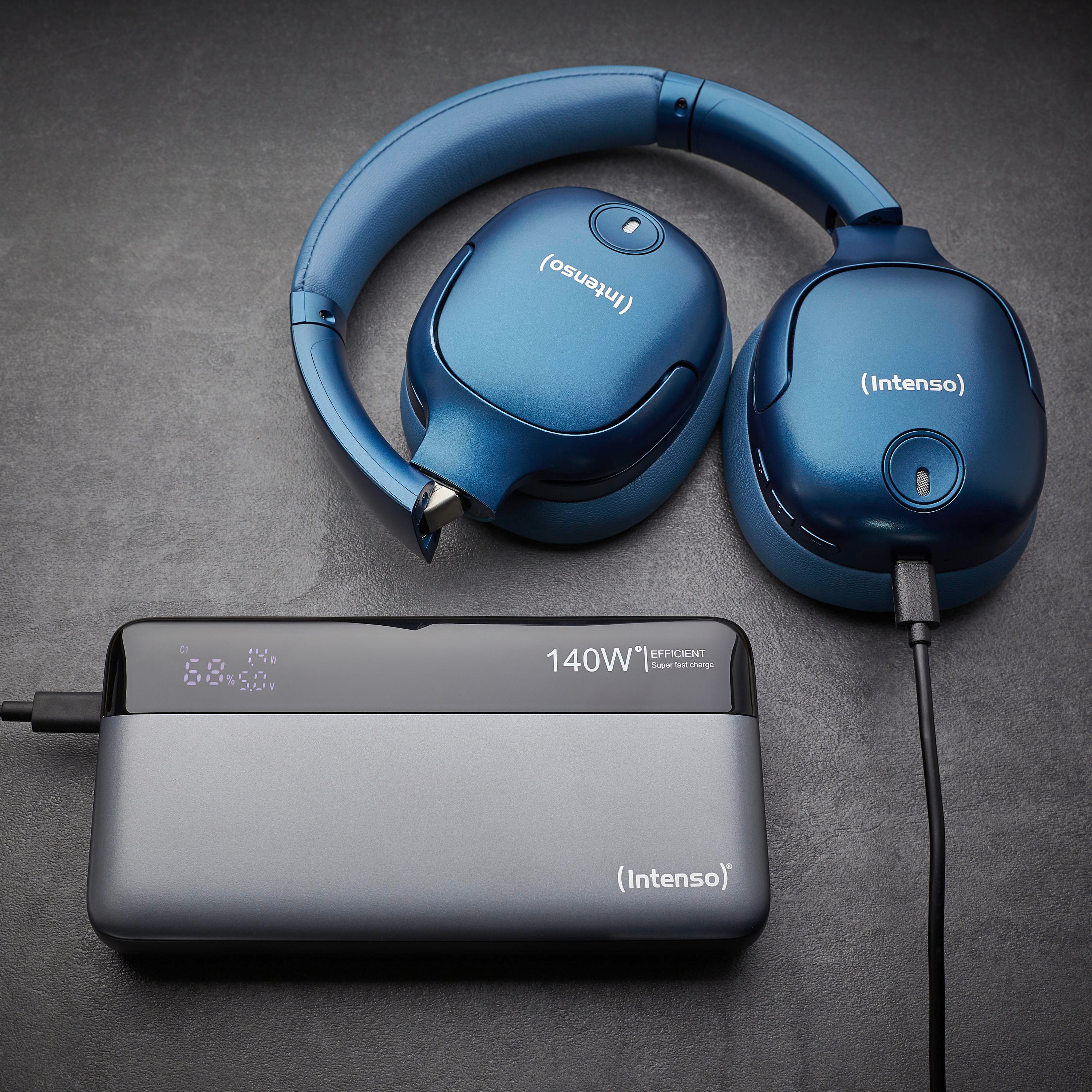 Blaue Kopfhörer und eine Powerbank liegen auf einer grauen Oberfläche. Die Powerbank zeigt den Ladestatus.