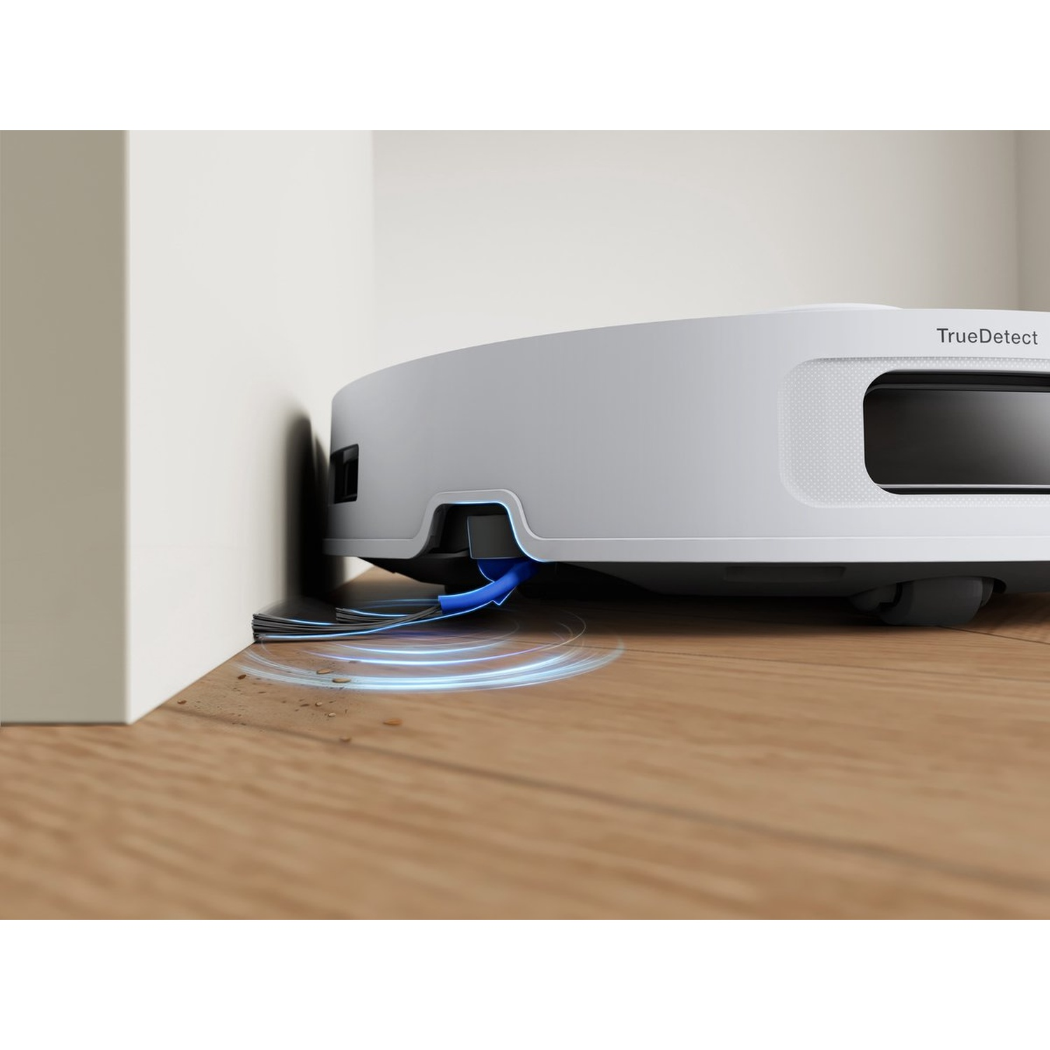 Een witte robotstofzuiger maakt een houten vloer schoon. De robot staat naast een muur. Blauwe lichtcirkels komen van de stofzuiger.