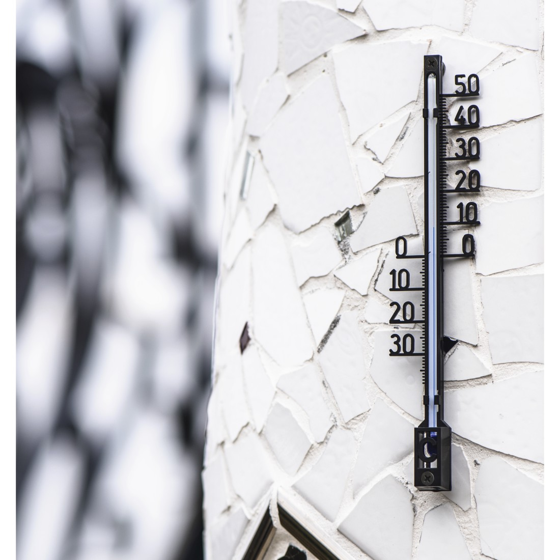 Ein schwarzes Thermometer ist an einer weiß gefliesten Säule befestigt. Das Thermometer zeigt ungefähr 10 Grad.