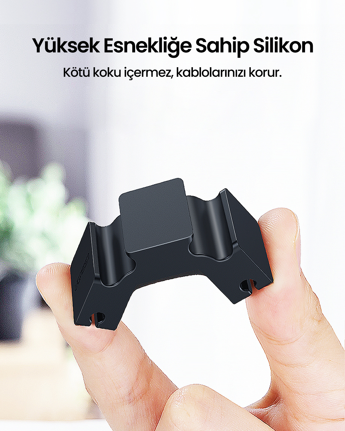 Siyah silikon bir kablo tutucu parmaklar tarafından tutuluyor. Dikdörtgen bir üst kısmı ve kavisli olukları var. Yukarıda metin var.