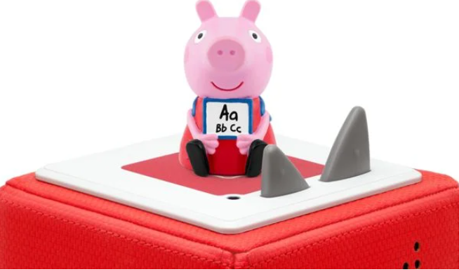 Rosa Peppa Wutz-Figur mit einem Schild mit ABC, auf einem rot-weißen Block mit grauen Haifischflossen.
