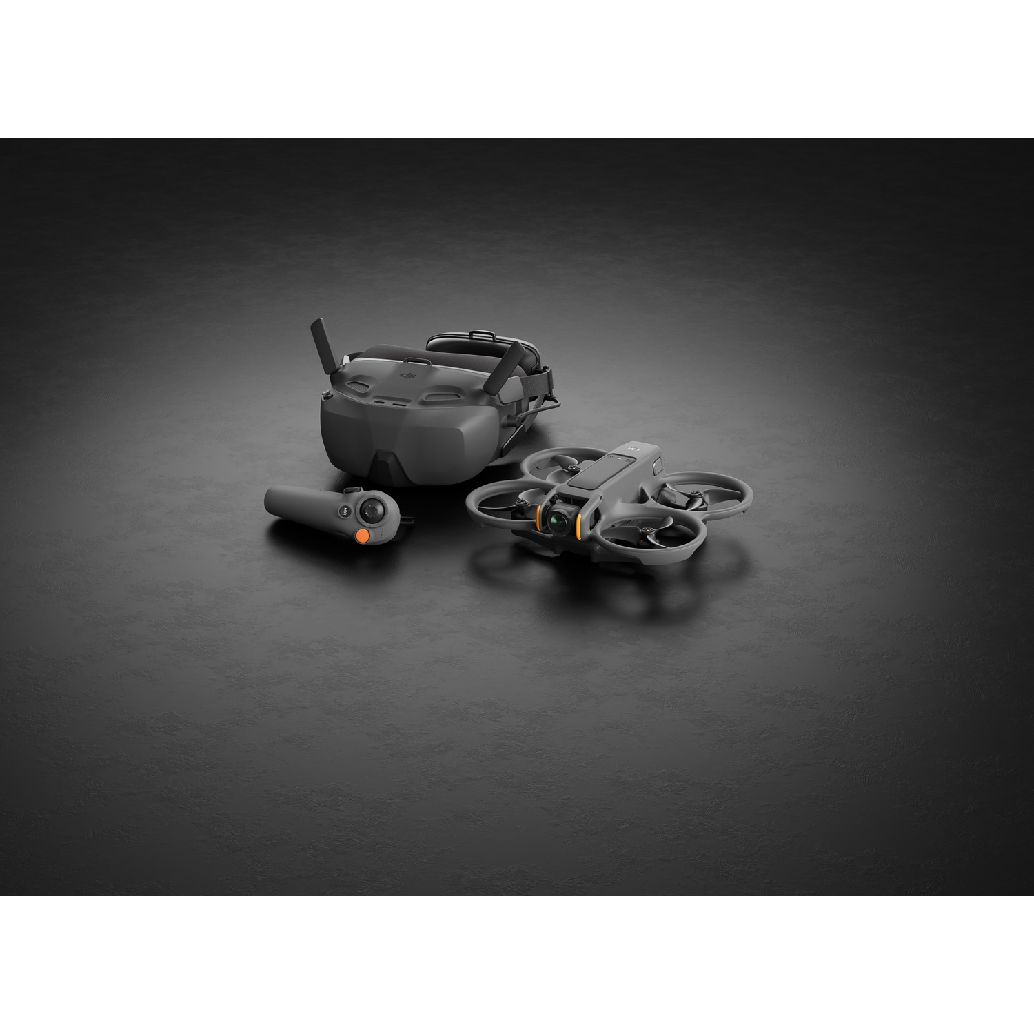 Un drone, une manette et un casque VR sont sur une surface sombre. Le drone est gris avec une caméra. La manette est petite.