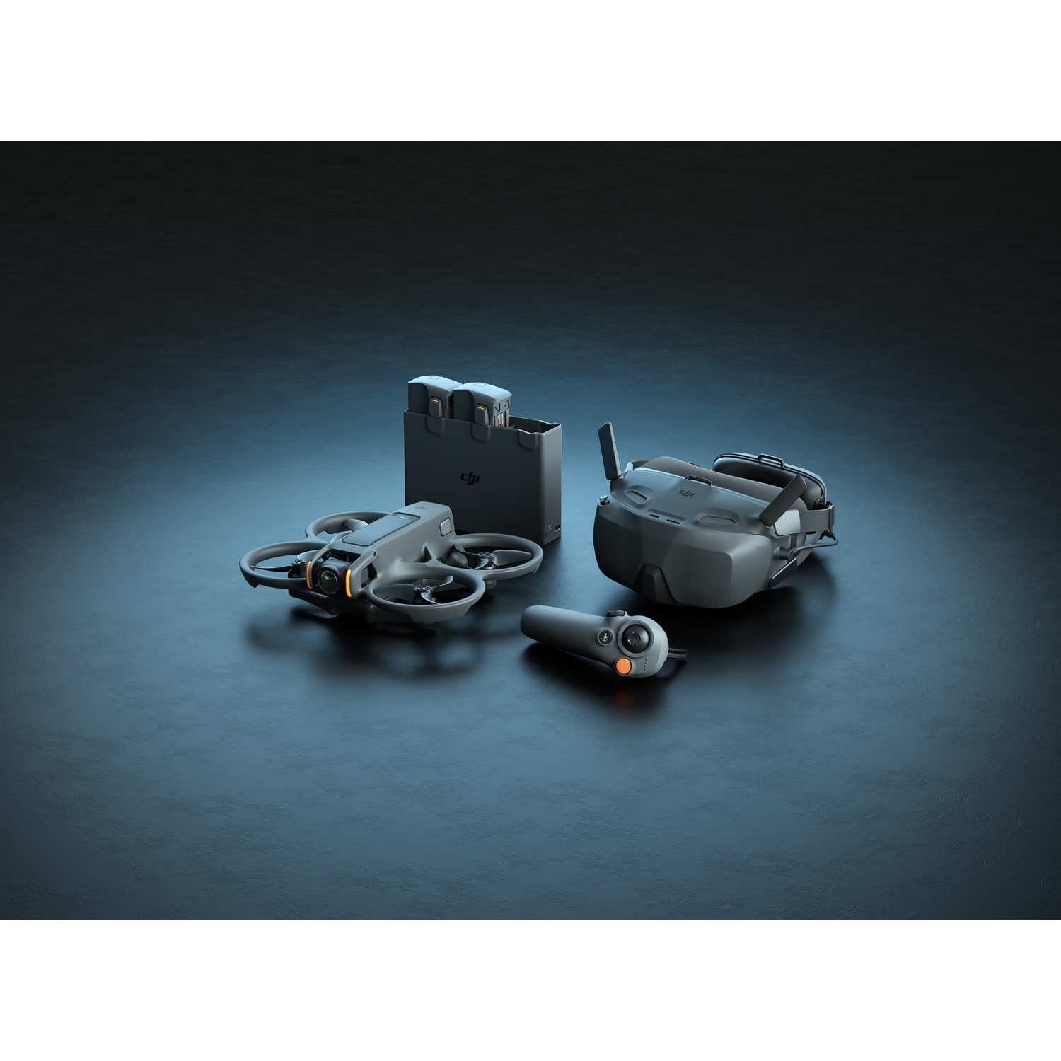 Een drone, controller, bril en batterijpack liggen op een donker oppervlak. De drone is grijs, de bril zwart en de controller grijs.