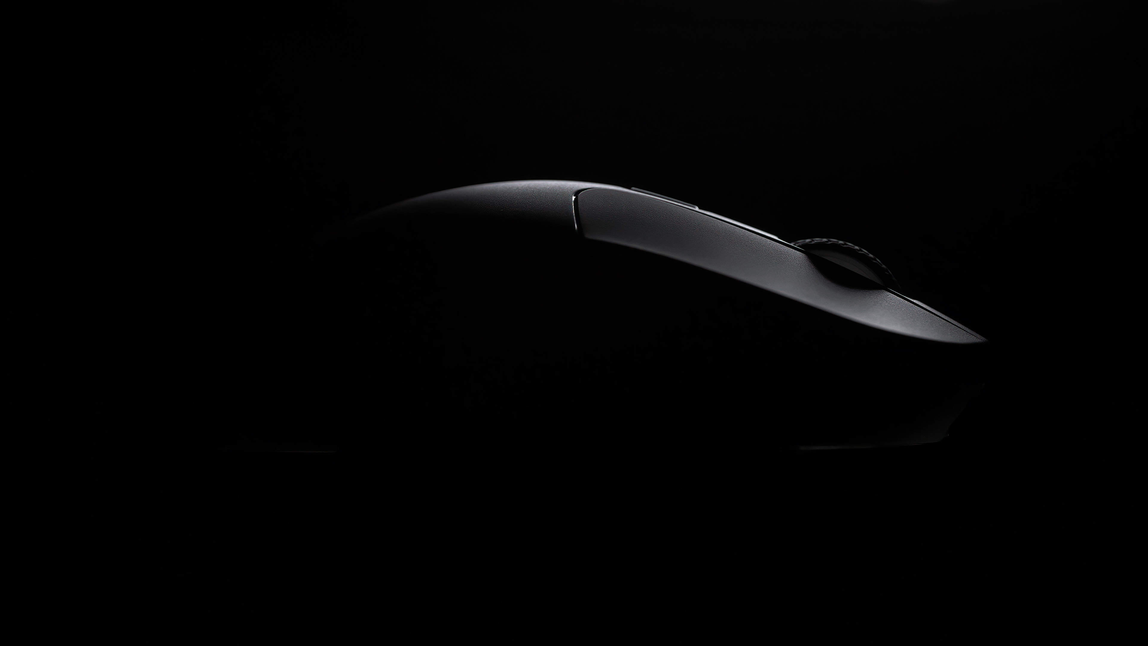 Eine schwarze Computermaus vor schwarzem Hintergrund. Die Maus ist leicht beleuchtet, wodurch ihre Form und das Scrollrad sichtbar werden.