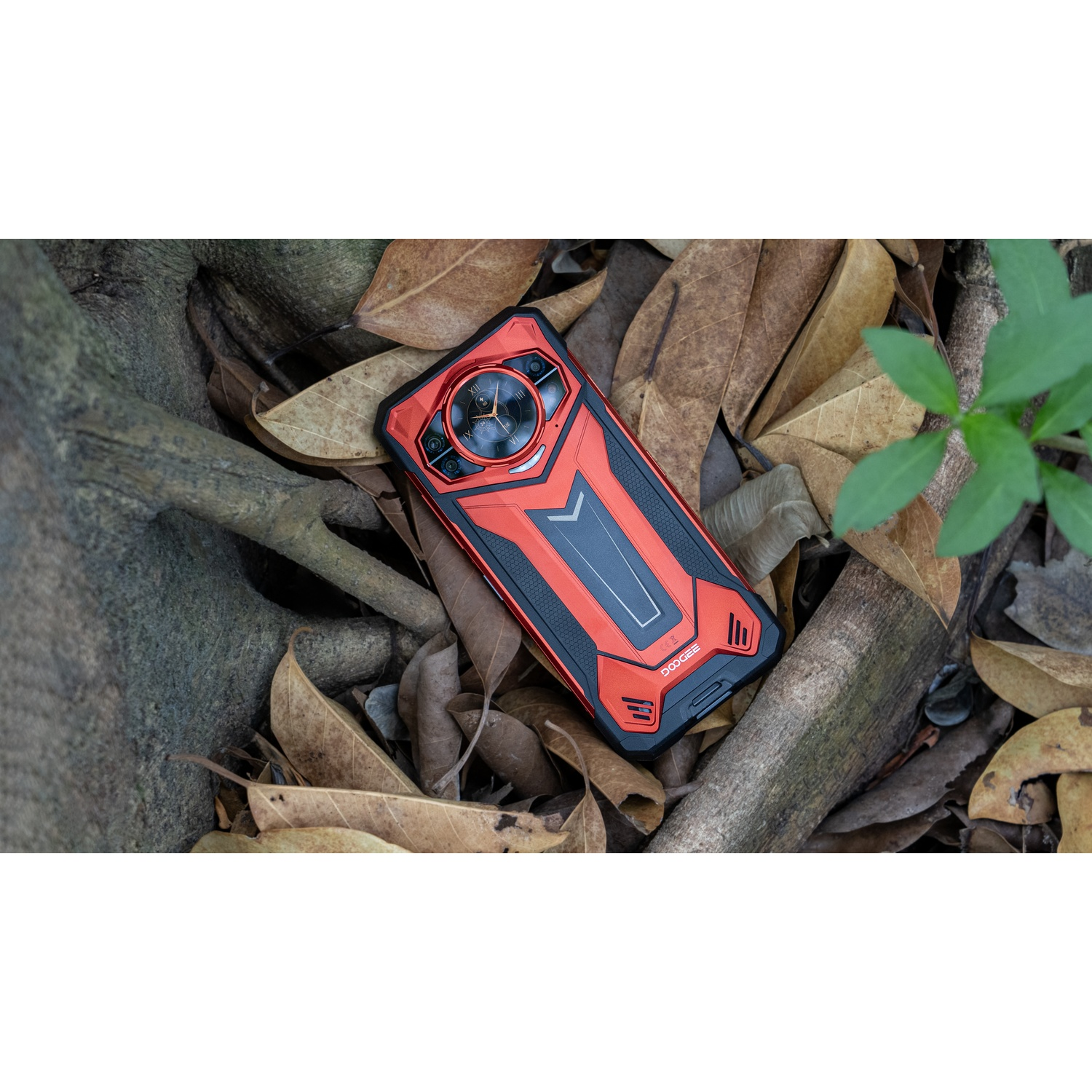 Telefono rosso e nero su foglie e rami. Il telefono ha un design distintivo con più fotocamere e un aspetto robusto.