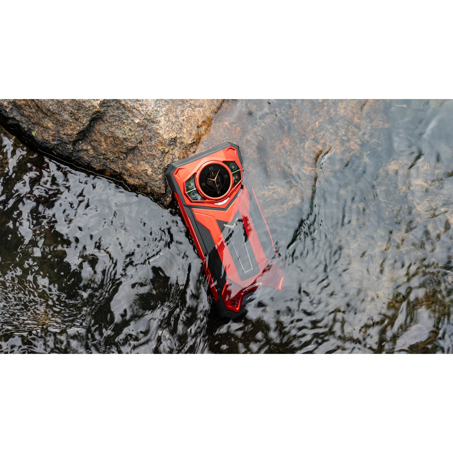 Uno smartphone rosso e nero è parzialmente immerso nell'acqua. Si trova vicino a una grande roccia con acqua corrente.
