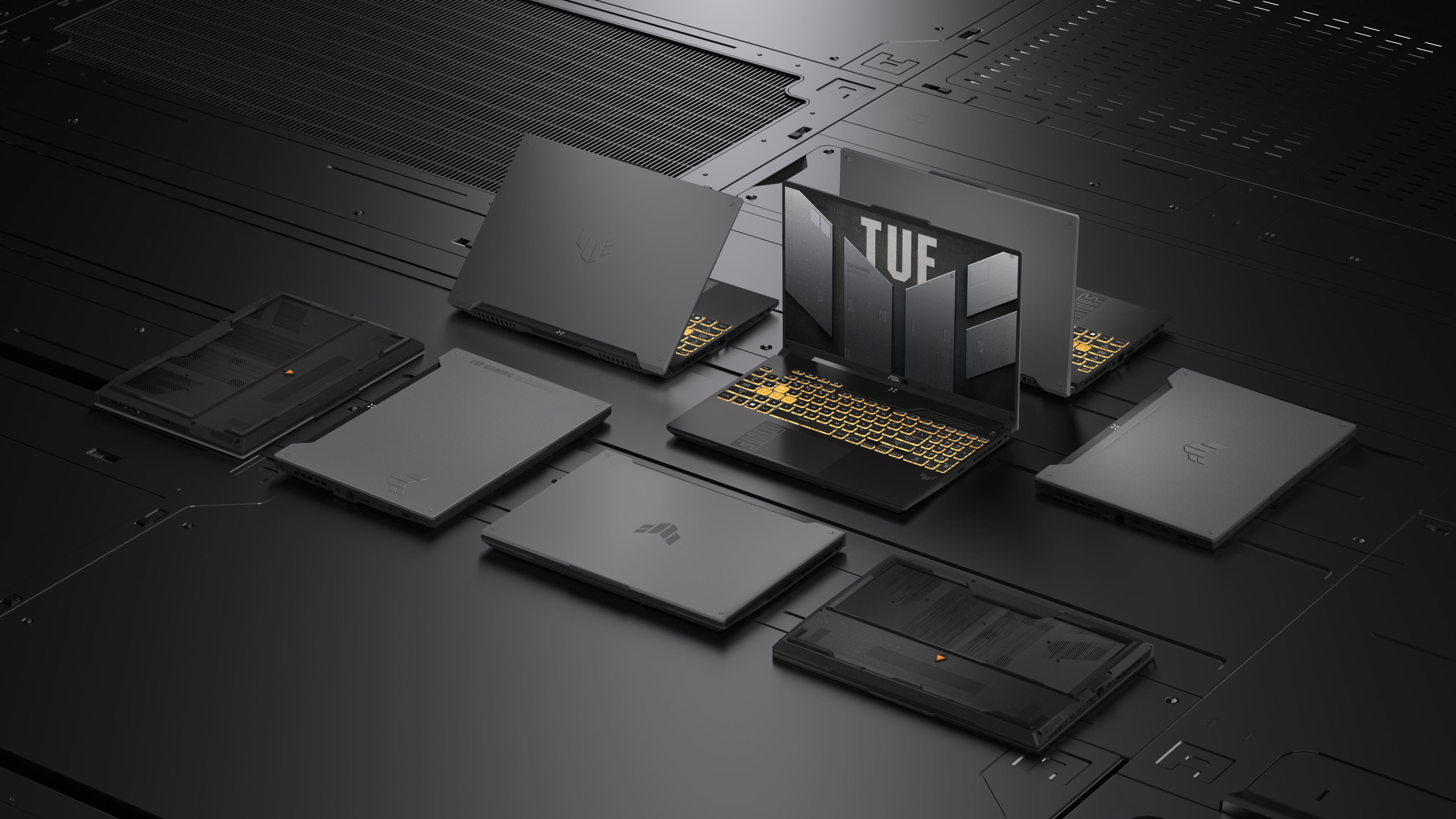 Verschillende grijze laptops liggen op een zwart oppervlak. Eén is open, met verlicht toetsenbord, anderen gesloten.