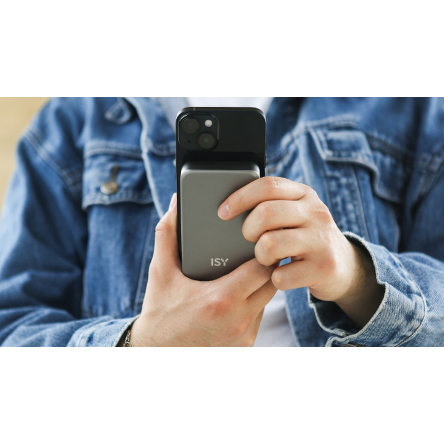 Una persona tiene in mano un telefono con una custodia nera e un power bank grigio. La persona indossa una giacca di jeans.