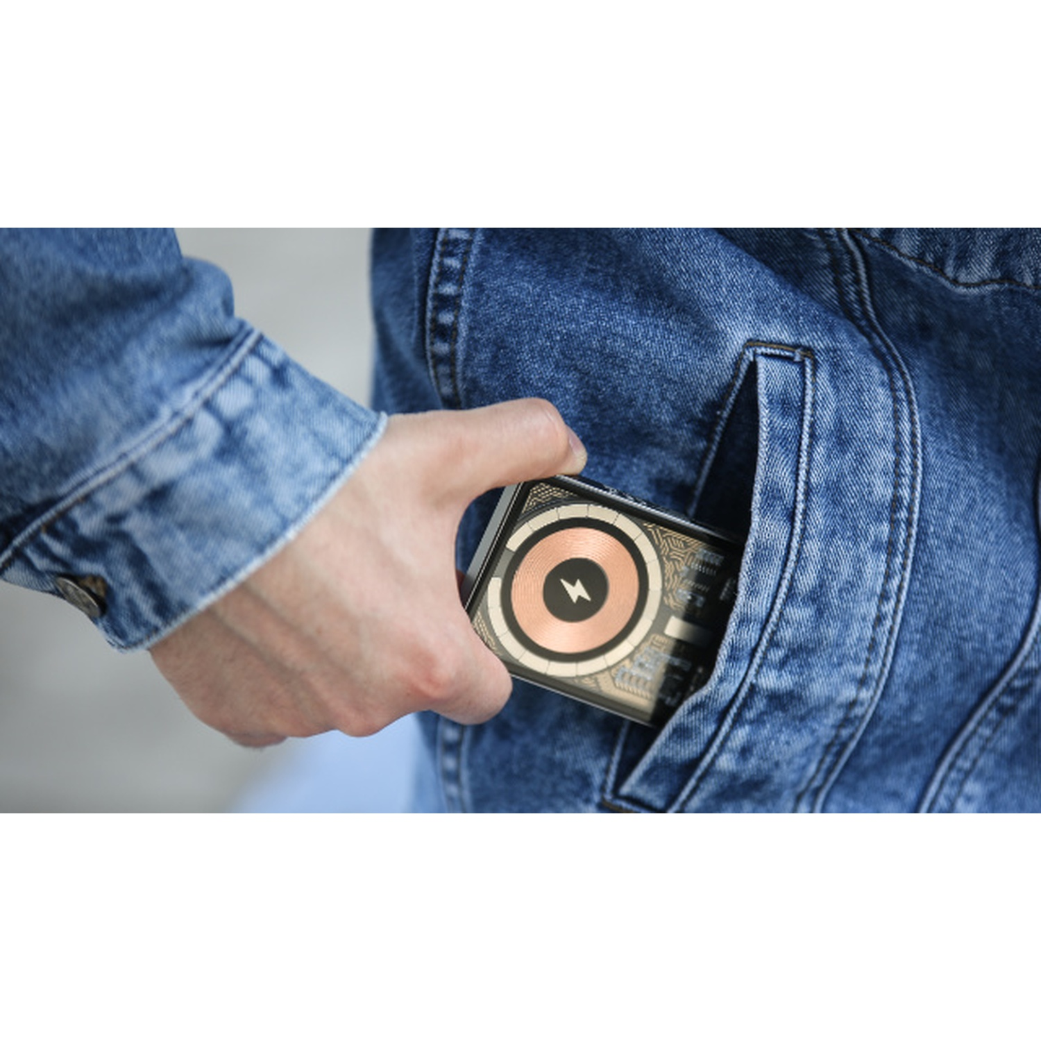 Una mano tiene in mano un dispositivo con un design a spirale in rame, infilandolo nella tasca di una giacca di jeans blu.