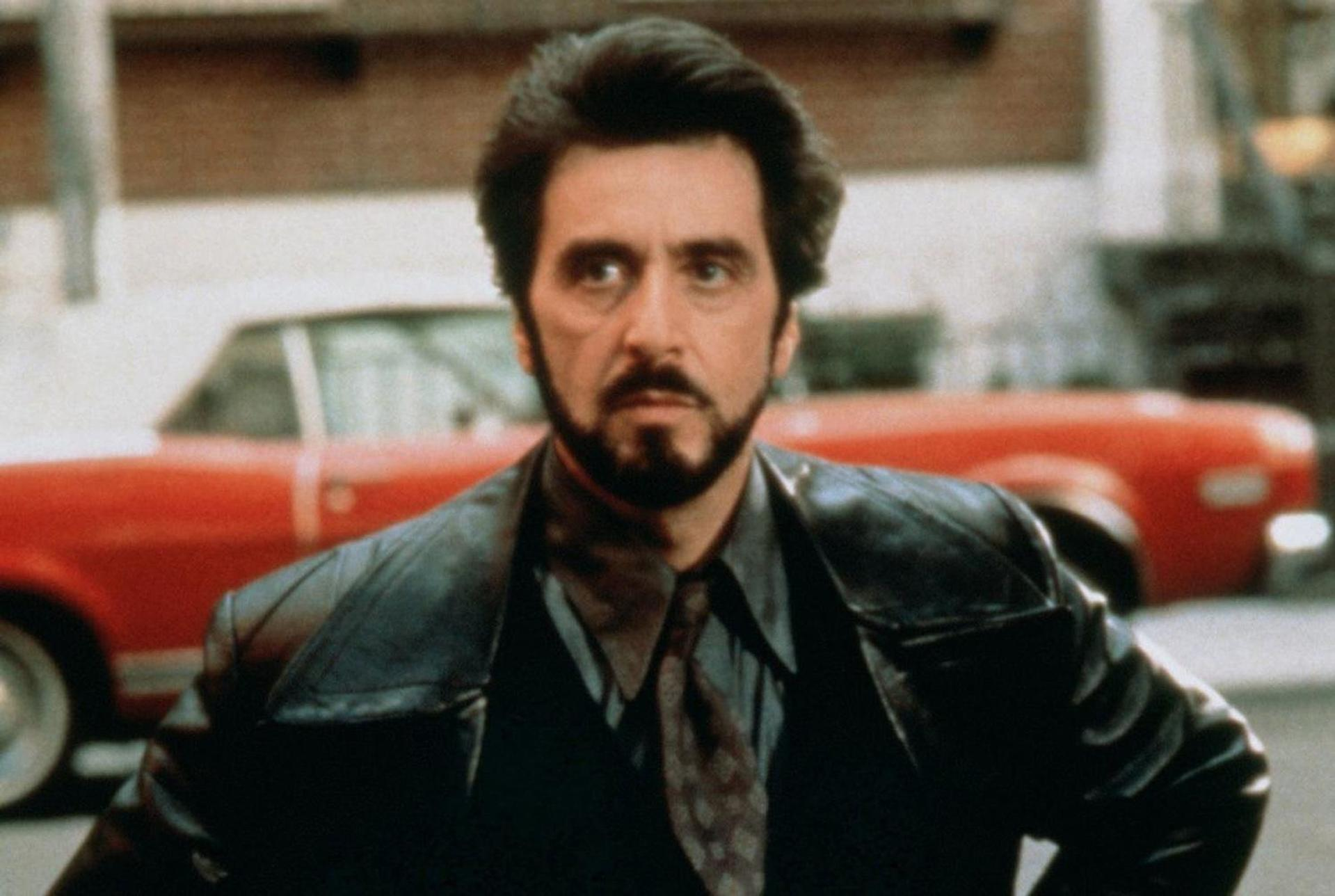 Al Pacino in Lederjacke, Krawatte und Bart. Im Hintergrund ein rotes Auto. Stadtkulisse.