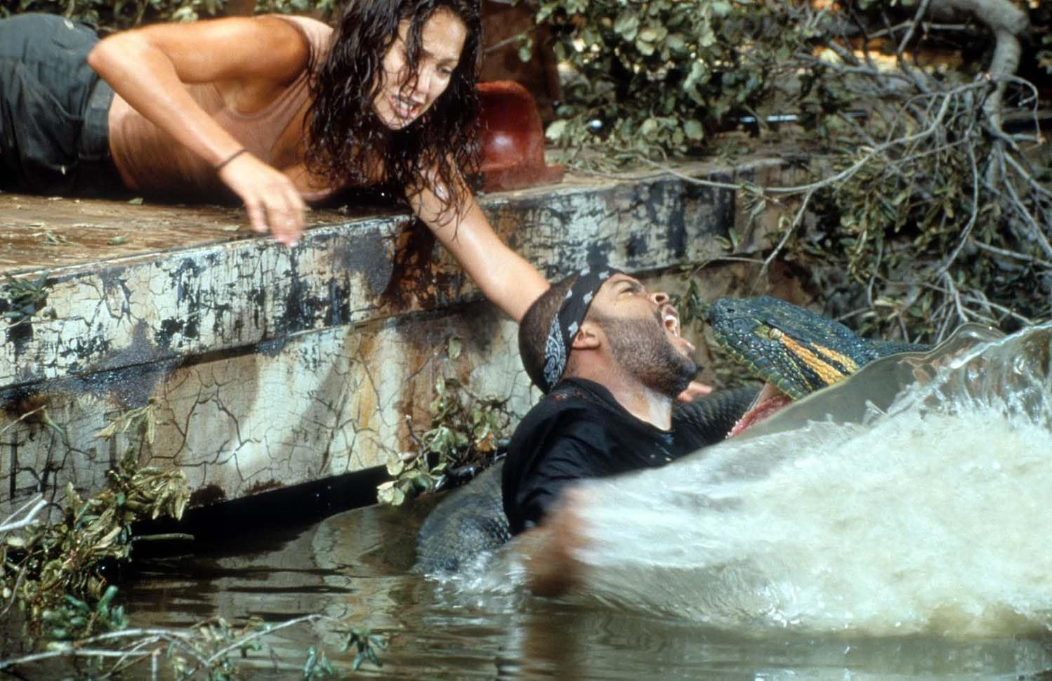 Eine Frau greift nach einem Mann, der im Wasser von einer großen Schlange angegriffen wird. Der Mann schreit. Der Kopf der Schlange ist sichtbar.