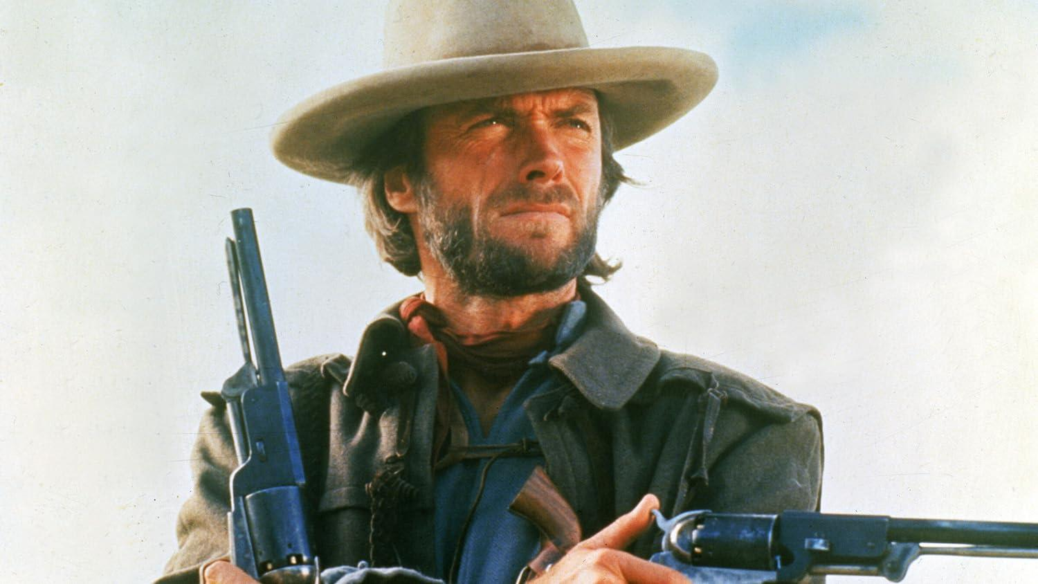 Clint Eastwood mit Cowboyhut, hält zwei Revolver. Er trägt ein blaues Hemd, einen roten Schal und einen langen Mantel, der ernst aussieht.